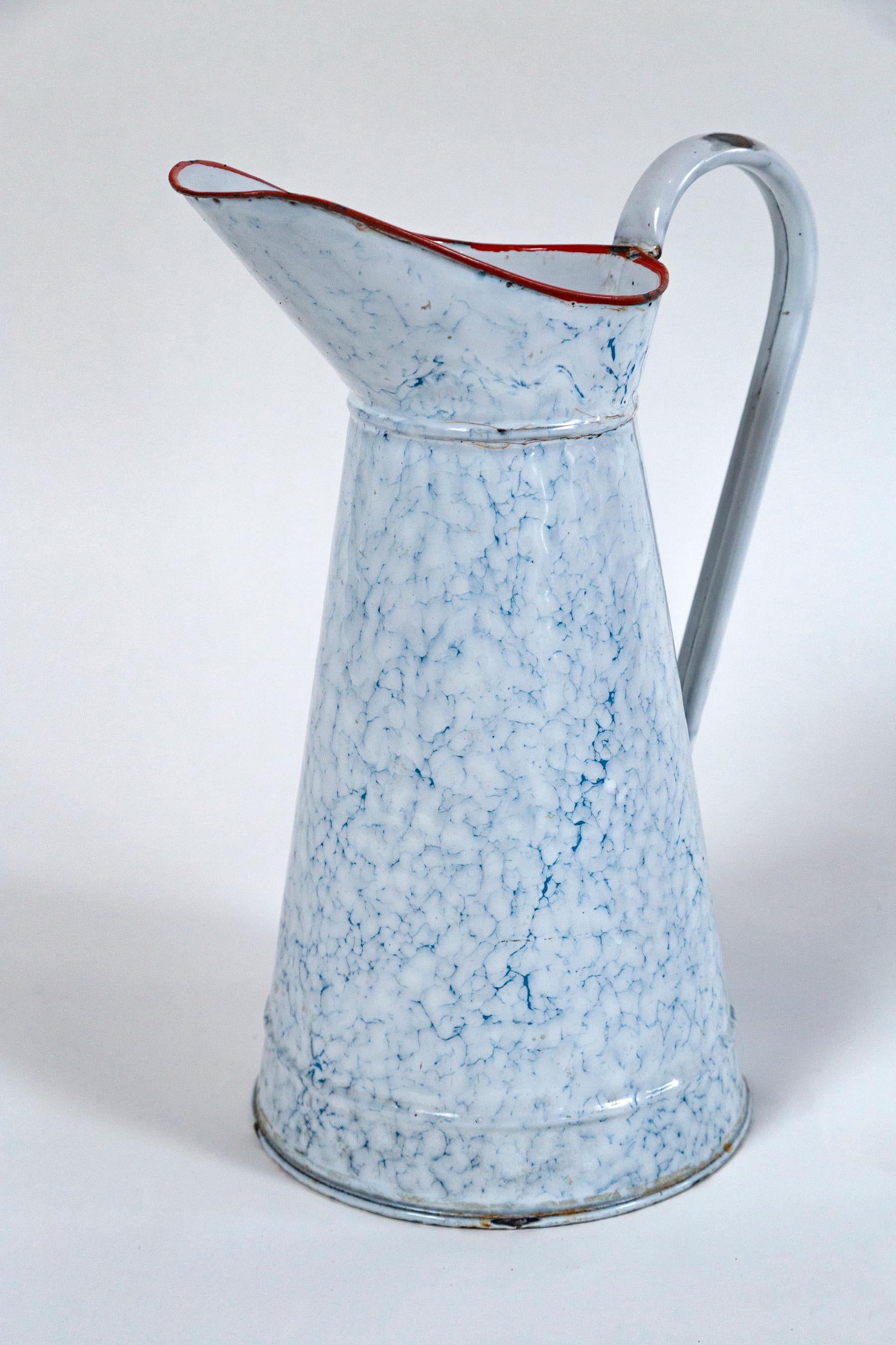 Vintage French blue and white Enamelware pitcher, circa 1920's. Tall, blue and white marbled pitcher with red rim.