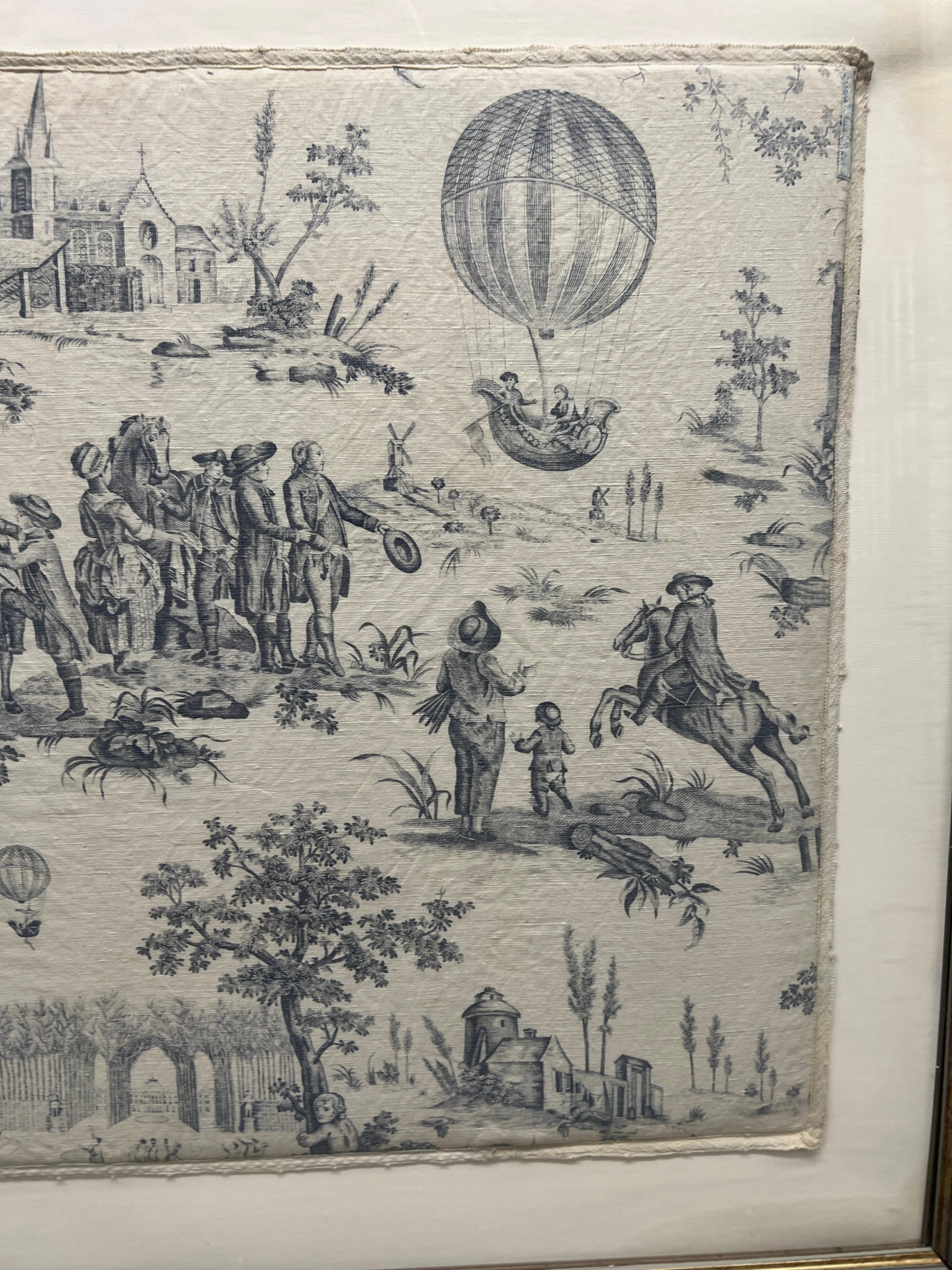 French, 20th century.

A vintage French Blue and White Toile De Jouy Framed Designer Fabric Panel. Showcasing traditional French figures parading horses, hot air balloons, buildings and more. The fabric is delicately set against a cream background