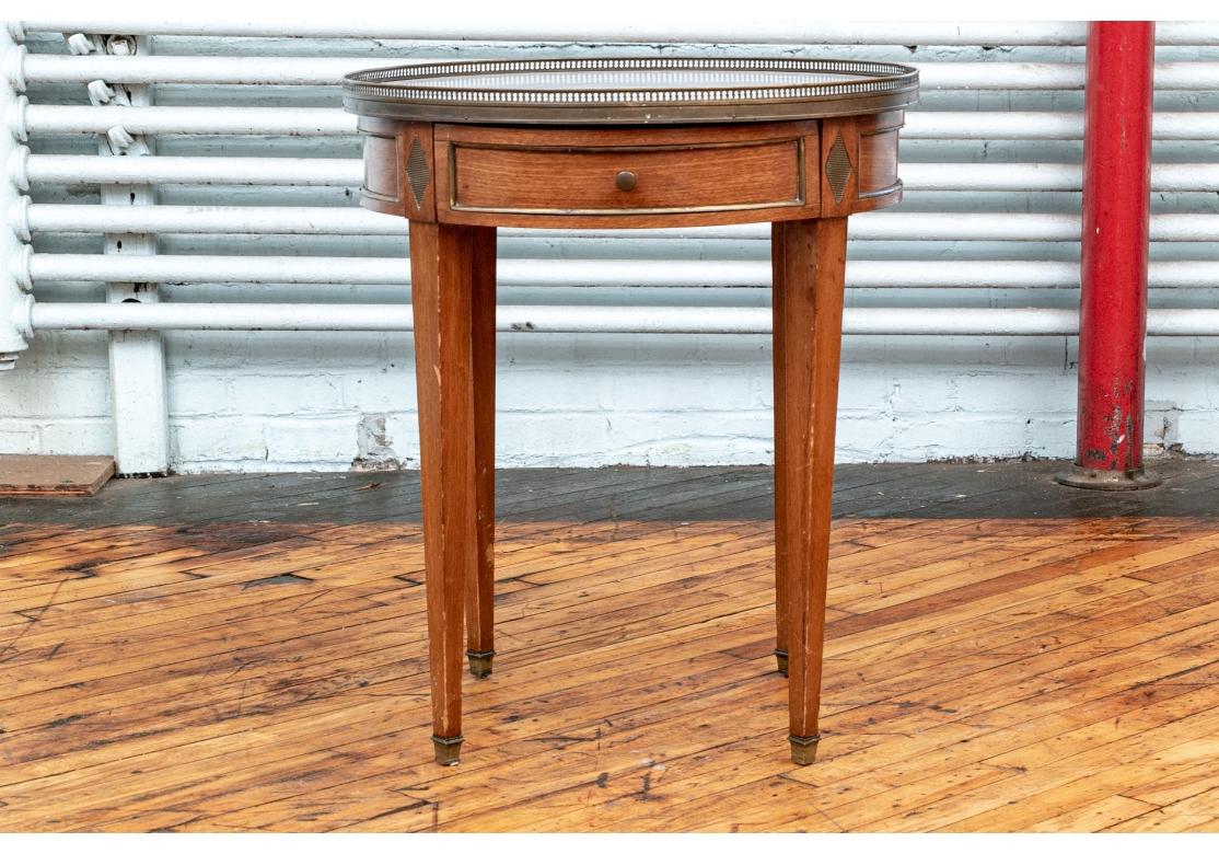 Fabriqué en France. Table bouillotte circulaire classique avec galerie en laiton autour du plateau en marbre gris. Le tablier de la table en acajou avec des moulures en laiton et un seul tiroir avec une tirette à bouton. Les pieds fuselés carrés