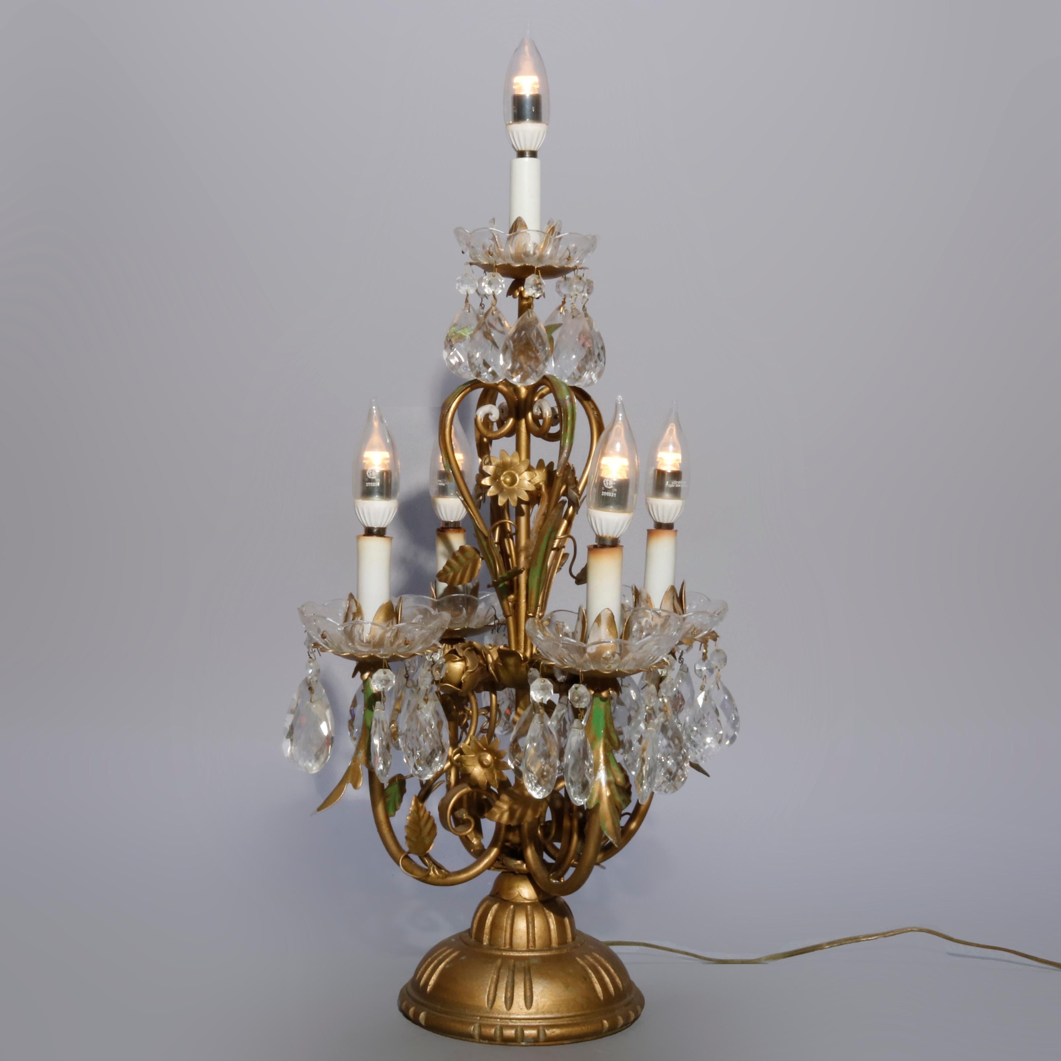 A vintage French candelabra table lamp offers brass frame with foliate and scroll arms and having hanging crystal prisms throughout, circa 1950

Measures: 26