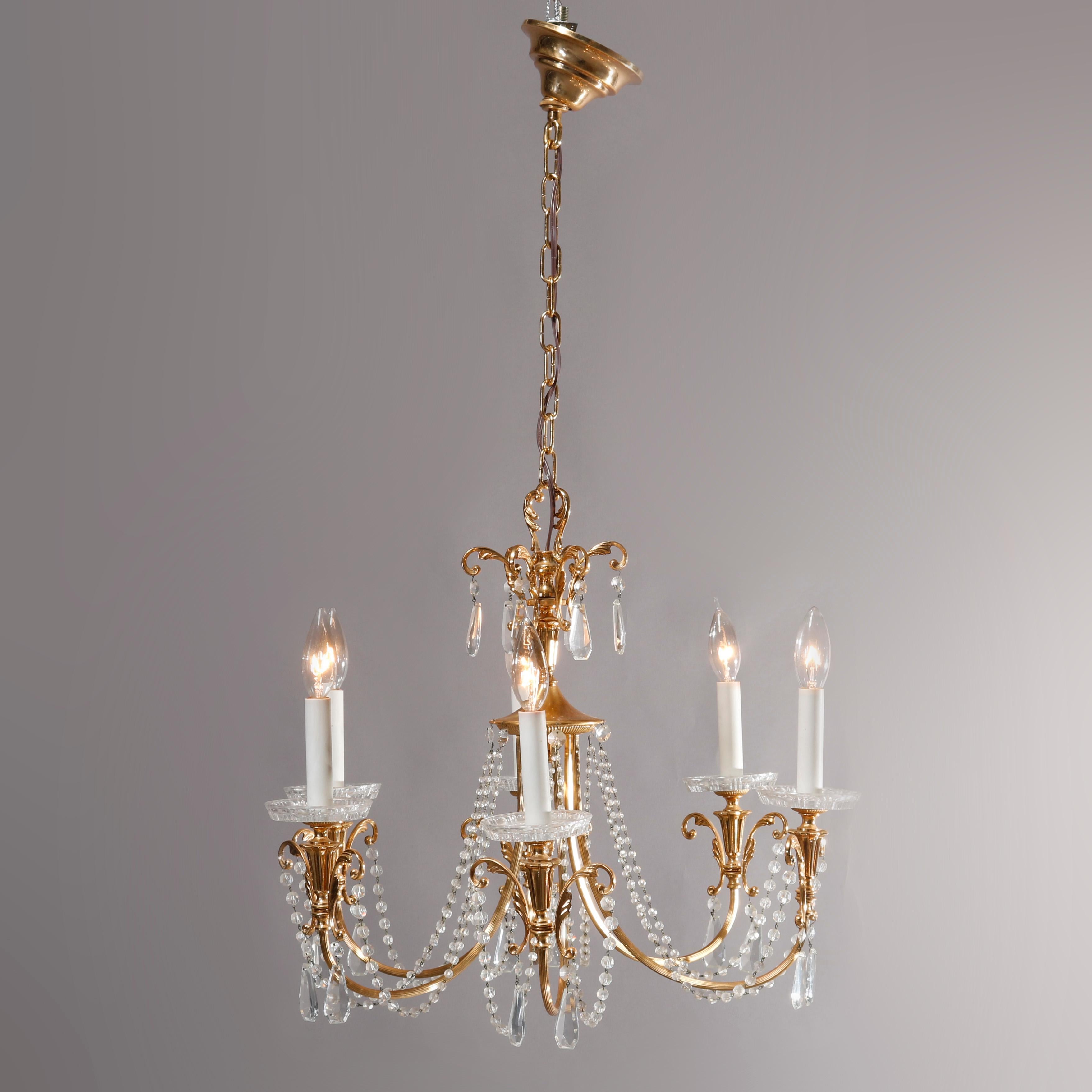 A vintage French chandelier offers brass frame with nine reeded C-scroll arms terminating in urn form and foliate elements having candle lights, strung and drop cut crystals throughout, wired for US electricity, circa 1930.

Measures: 41