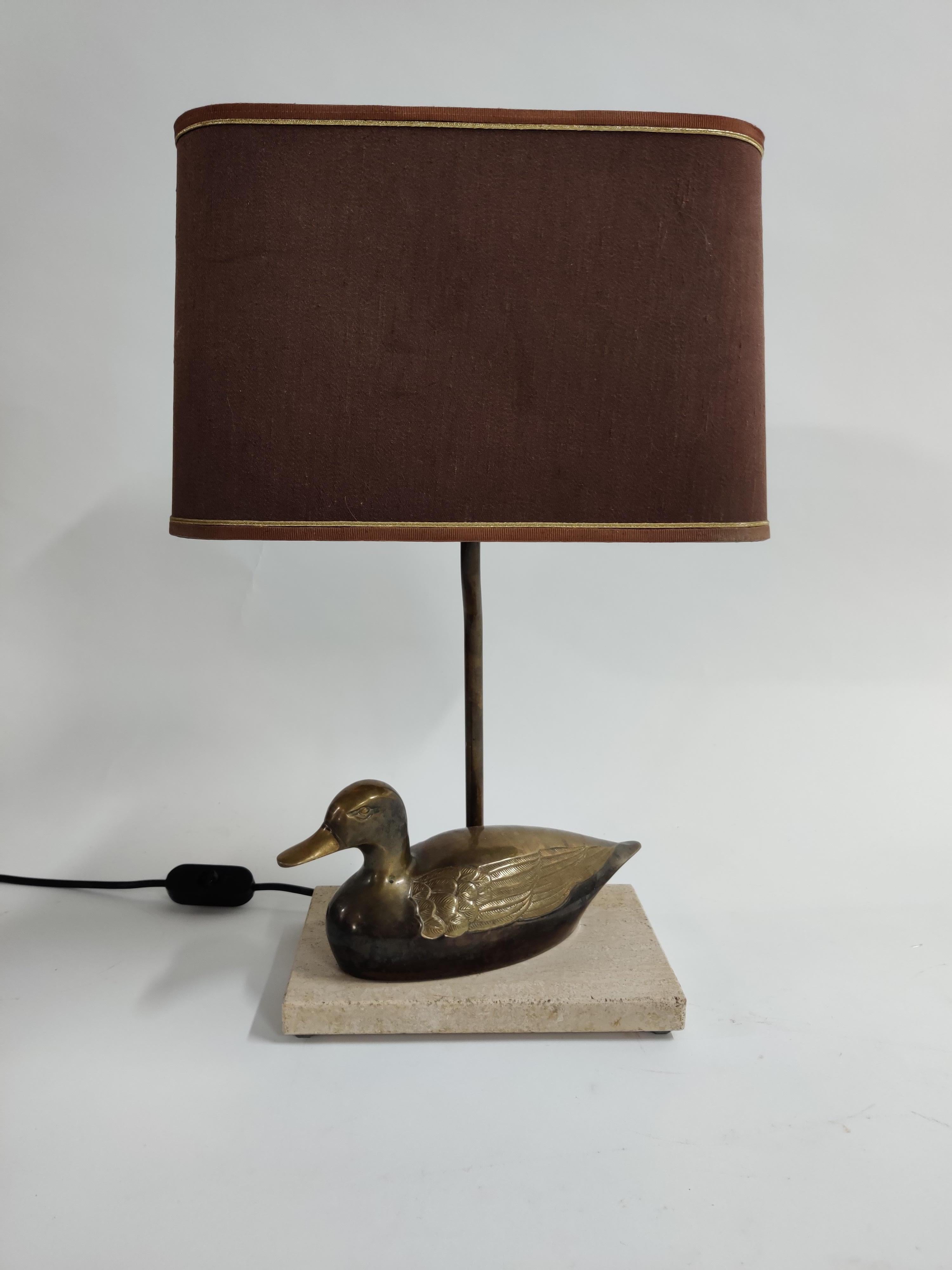 Brass duck table lamp which is mounted on beige travertine base. 

Unique piece. This lamp emits a very warm light, 

1970s, France

Very good condition, no damages.

Delivered with the original shade.

Dimensions:
Height: