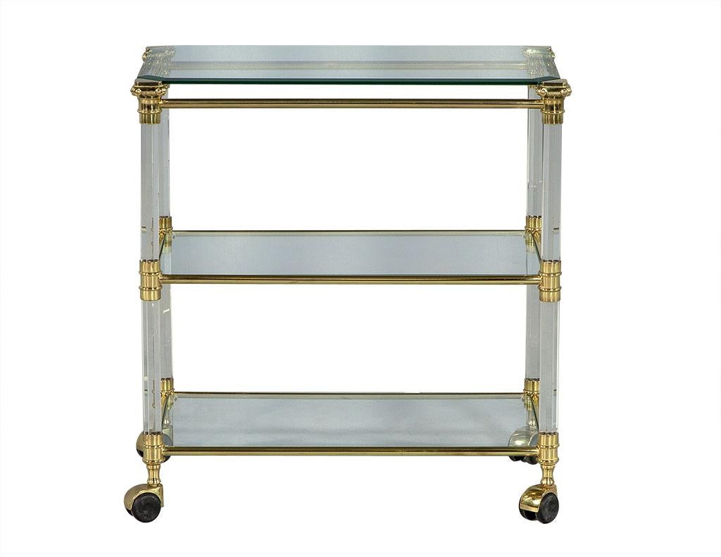 Vintage French brass glass and Lucite serving cart. 1970s Hollywood Regency style serving cart with three glass shelves on castors. Octagonal shaped Lucite supports accented with detailed brass connectors and trim. Original from France.