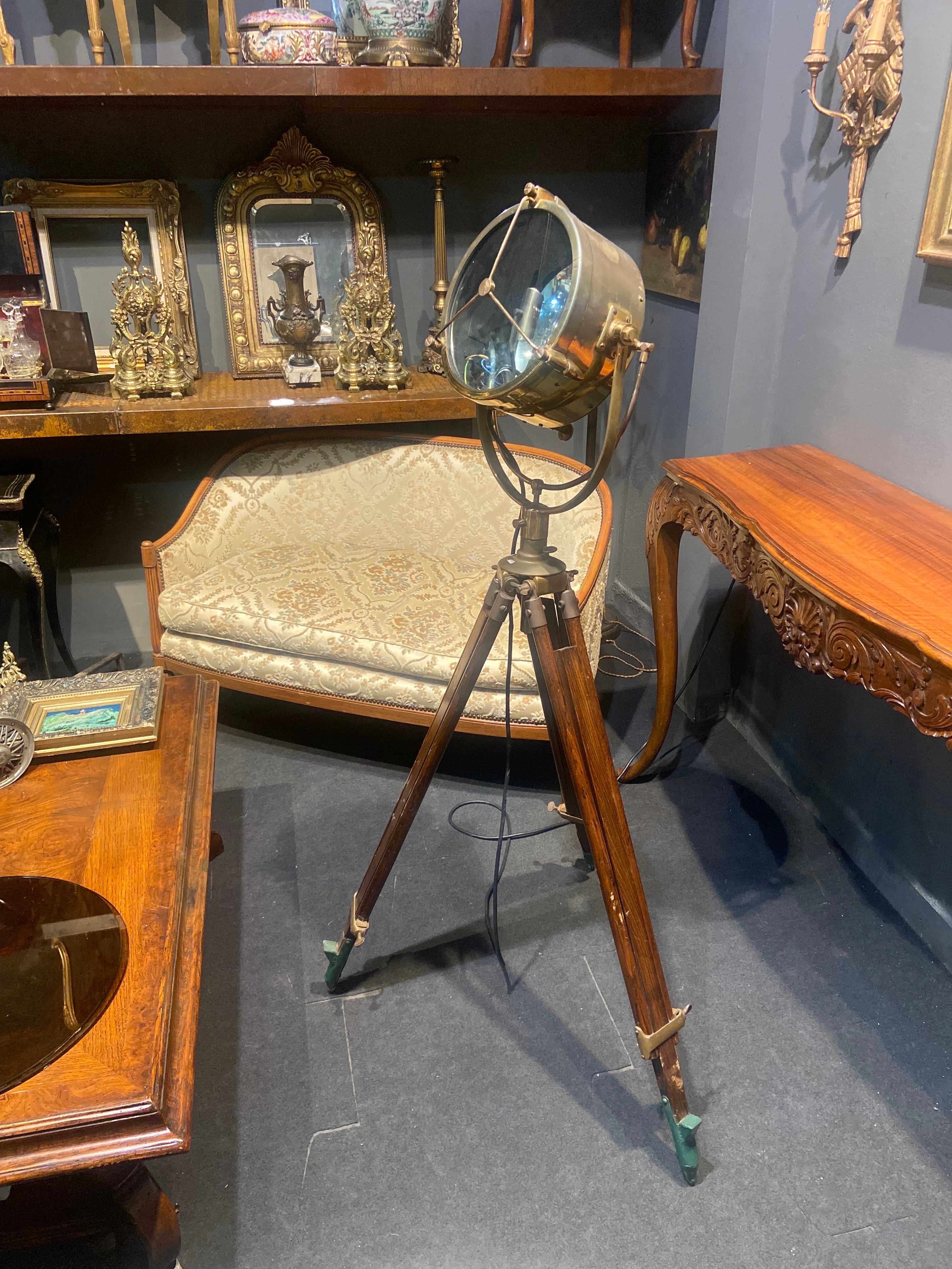 20th century English vintage brass search lamp paired with a wooden antique surveyors tripod, to create a stunning floor lamp. The overall condition is very good only the round mirror behind the bulb is broken.
The wooden tripod legs could be