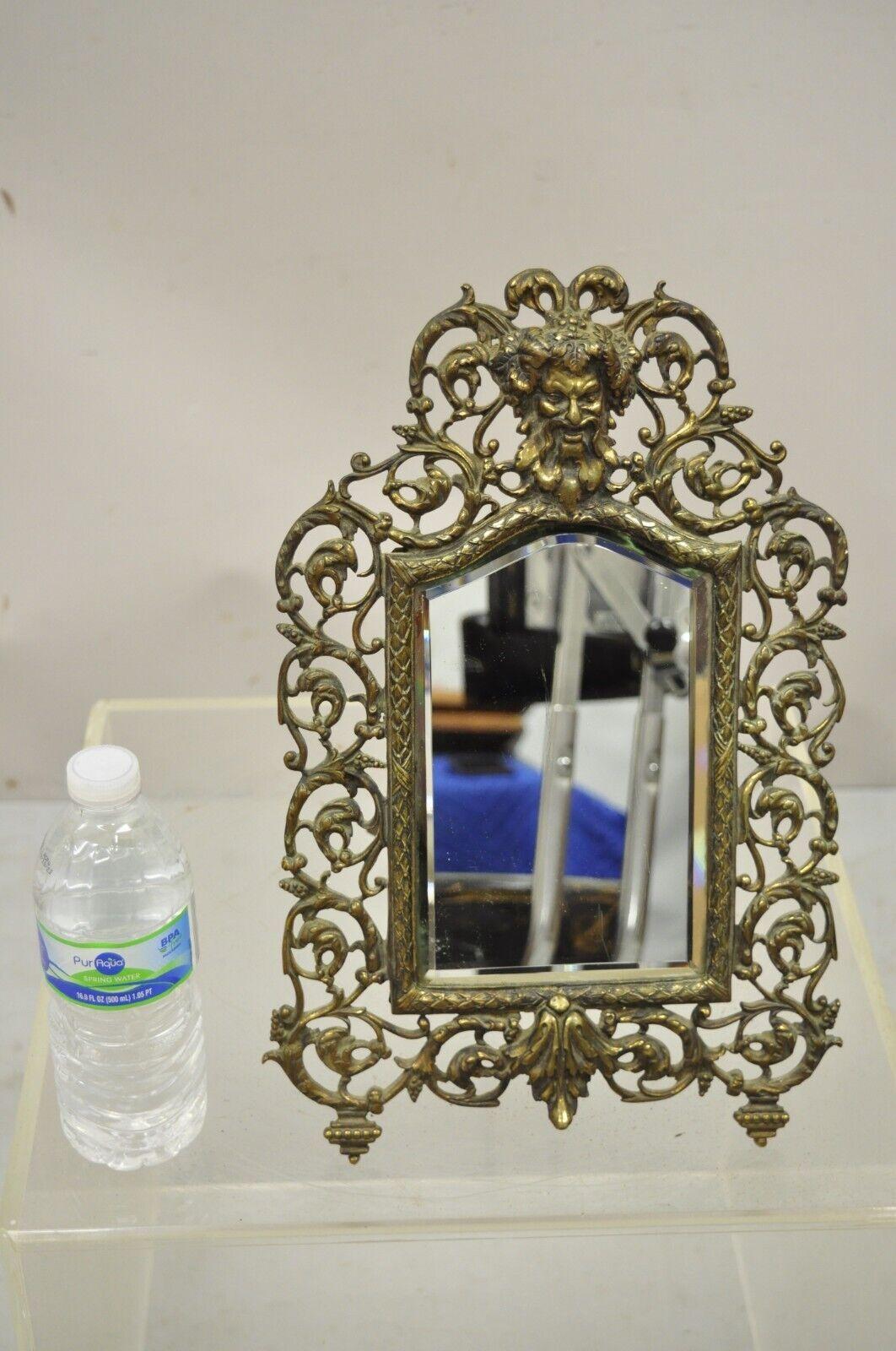 Vintage French brass small beveled glass vanity shaving mirror with bacchus face. Item features an ornate brass frame with Bacchus face and pierced leafy scrolls, beveled glass mirror, nice smaller table top size. Circa Early to mid 20th century.