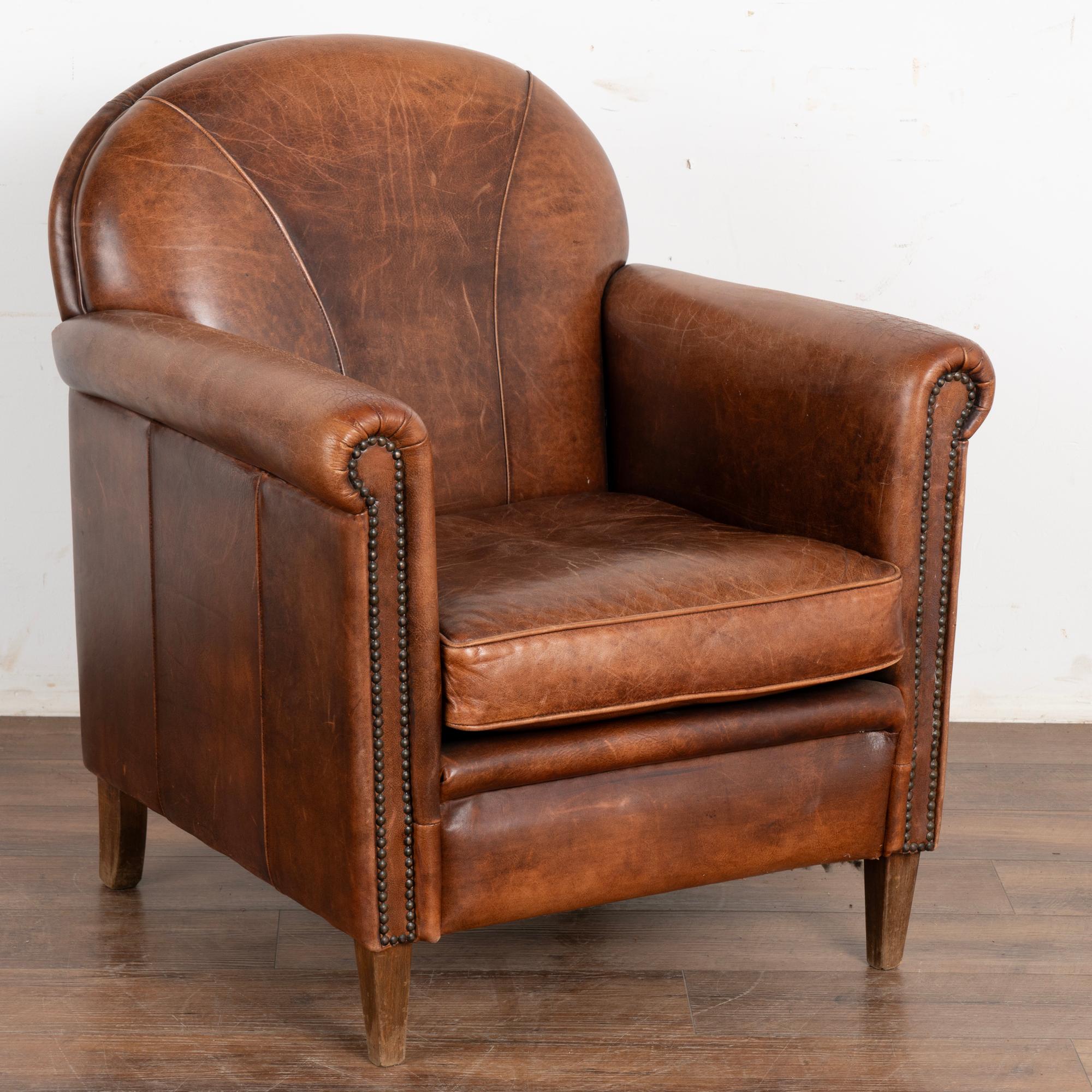 Vintage brown leather club arm chair with hard wood legs; seam details add visually to back and sides.
Upholstered in vintage sheep's leather with rich patina, rolled arms and nail head trim.
Sold in original vintage condition; solid/stable and sits