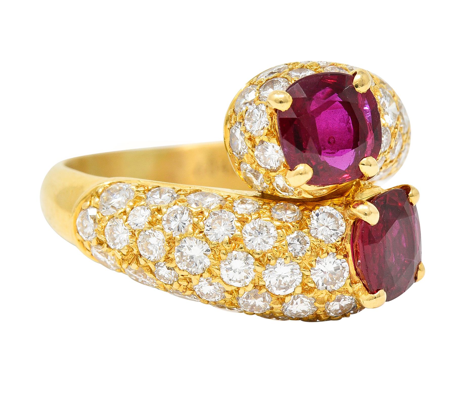 Bypass ring features two round cut Thai rubies weighing collectively approximately 1.90 carats. Very well matched in vivid red color - eye clean. Prong set atop bombè formed shoulders pavè set throughout by round brilliant cut diamonds. Weighing in