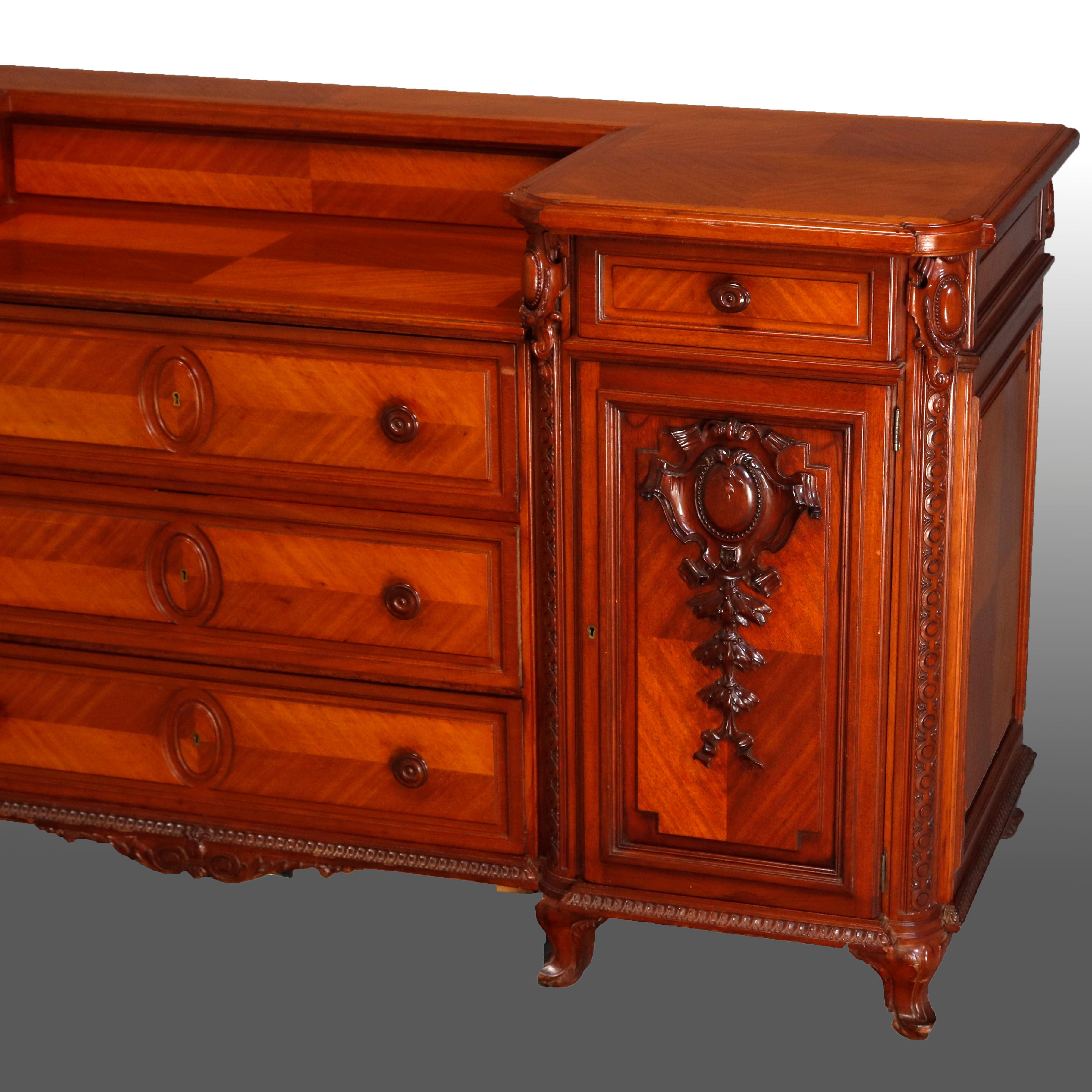 A vintage French sideboard offers mahogany construction with bookmatched satinwood throughout and drop-center top surmounting three central long drawers flanked by cabinets each opening to three pull-out drawers and having carved trim with shield