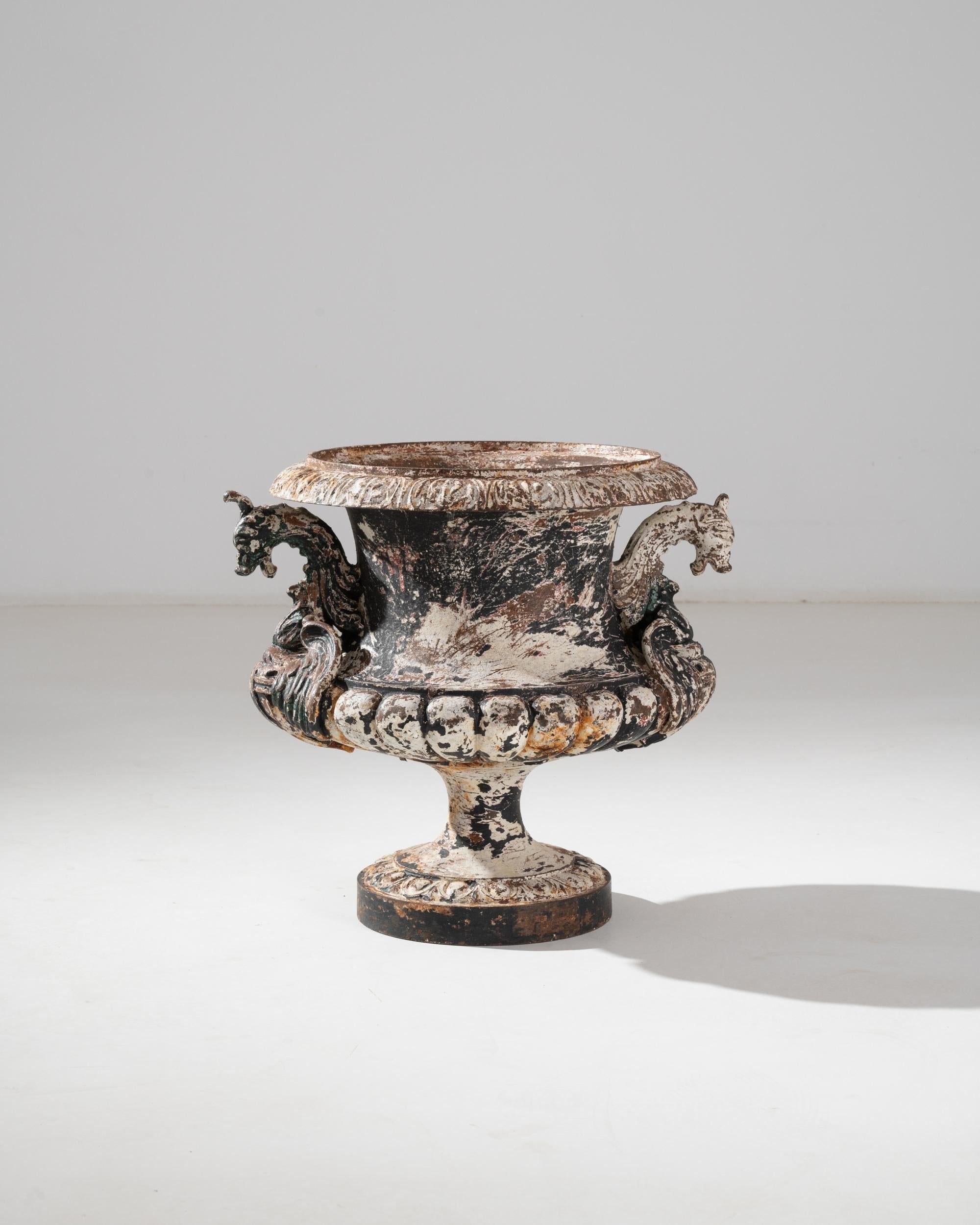 A cast iron planter from France, made in the 19th century. The campana shape resembled an upturned bell with a fluted cupola and broad lip, reminiscent of an opening blossom. Fantastic creatures make intruiging handles on either side of the urn.