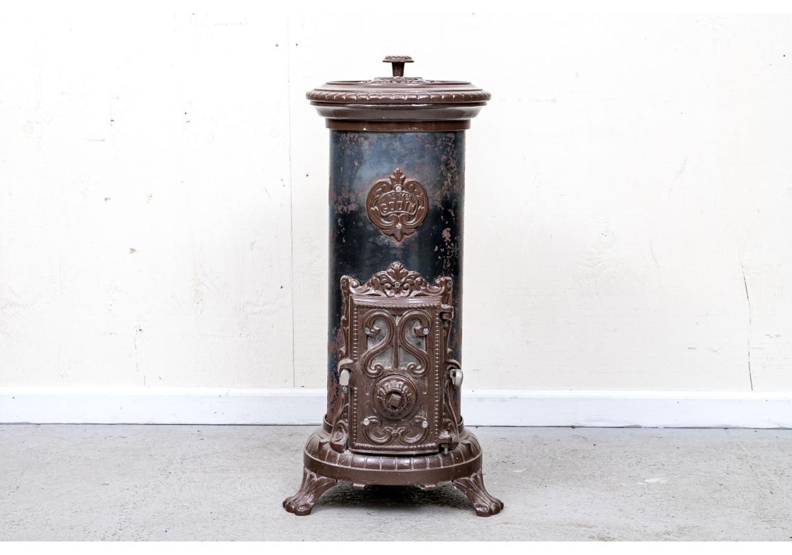 A small scale circular cast iron stove by a major French manufacturer. The metal cylinder is in green-gray paint and the iron pierced top, the door and other attachments are in dark brown enamel. Raised on scrolled feet. Along with a small demilune
