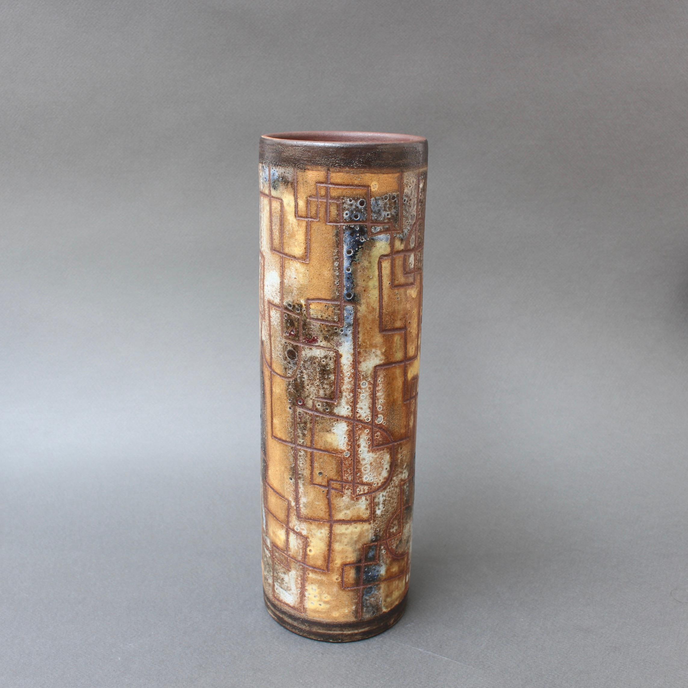 Vintage ceramic flower vase by Alexandre Kostanda (circa 1960s). The cylindrical vase presents a misty appearance with natural earth tones in brown, beige with surprises in blue hues. Incised lines randomly placed create visual interest and are