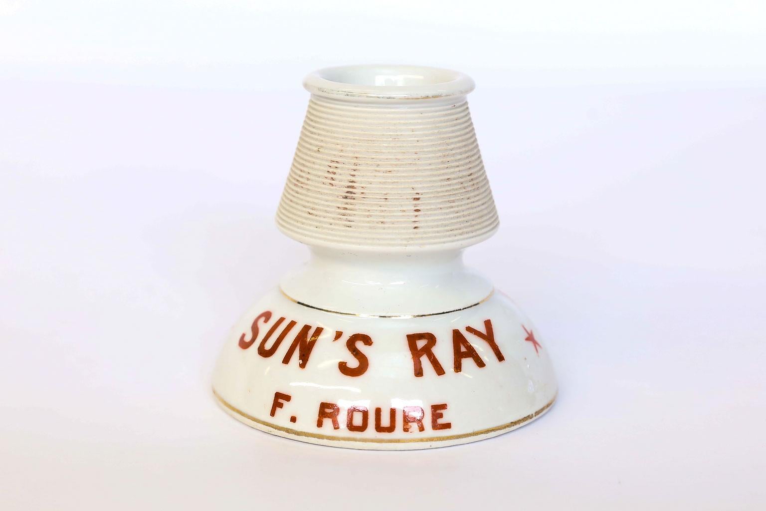 This is a French match holder and striker of white porcelain with burnt orange advertising around the base and two gold stripes. The advertising reads Le Goudron, F. Roure on one side and Sun's Ray, F. Roure on the other side. The maker's mark in