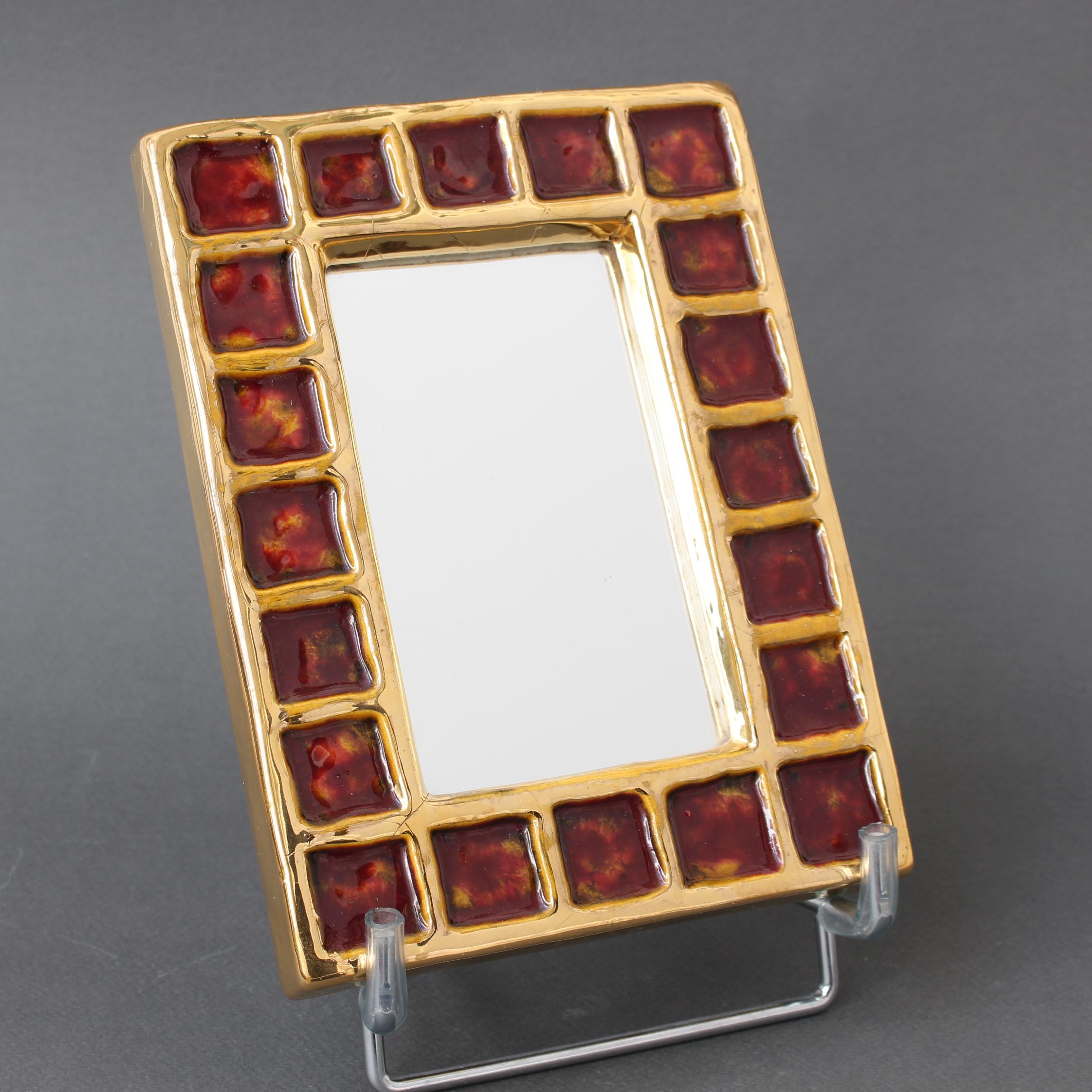 French vintage ceramic wall mirror by François Lembo (circa 1970s). A whimsically decorated, small rectangular wall mirror with gold coloured inner and outer borders framing a series of reddish-brown enamel squares which seem filled like a luxurious