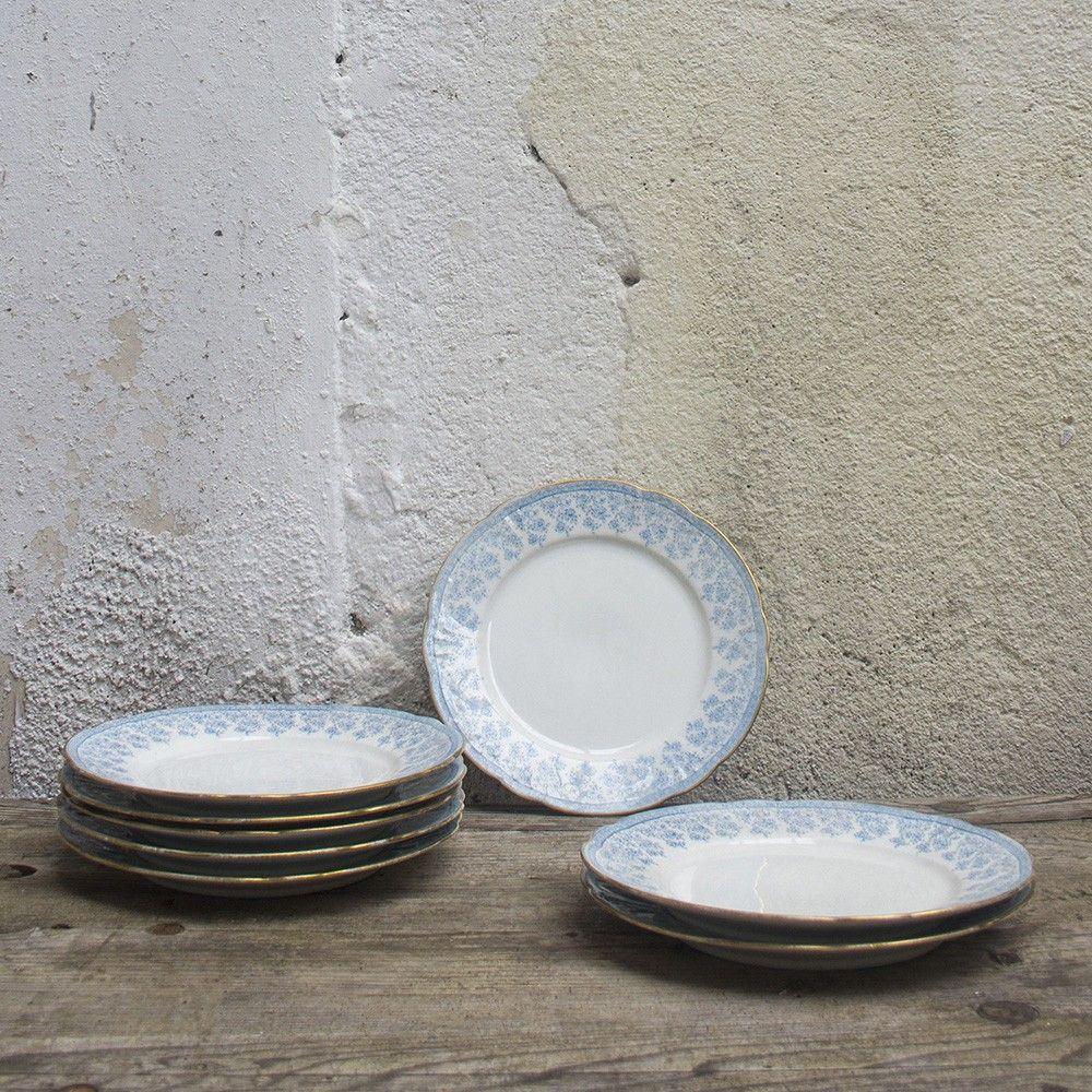 This set of Ceramic tableware was manufactured by WM Guérin & Co. in Limoges, France between 1900-1930. Each plate is a white cream ceramic base with light blue floral motifs bordering the center. The edges have been finished in gold.