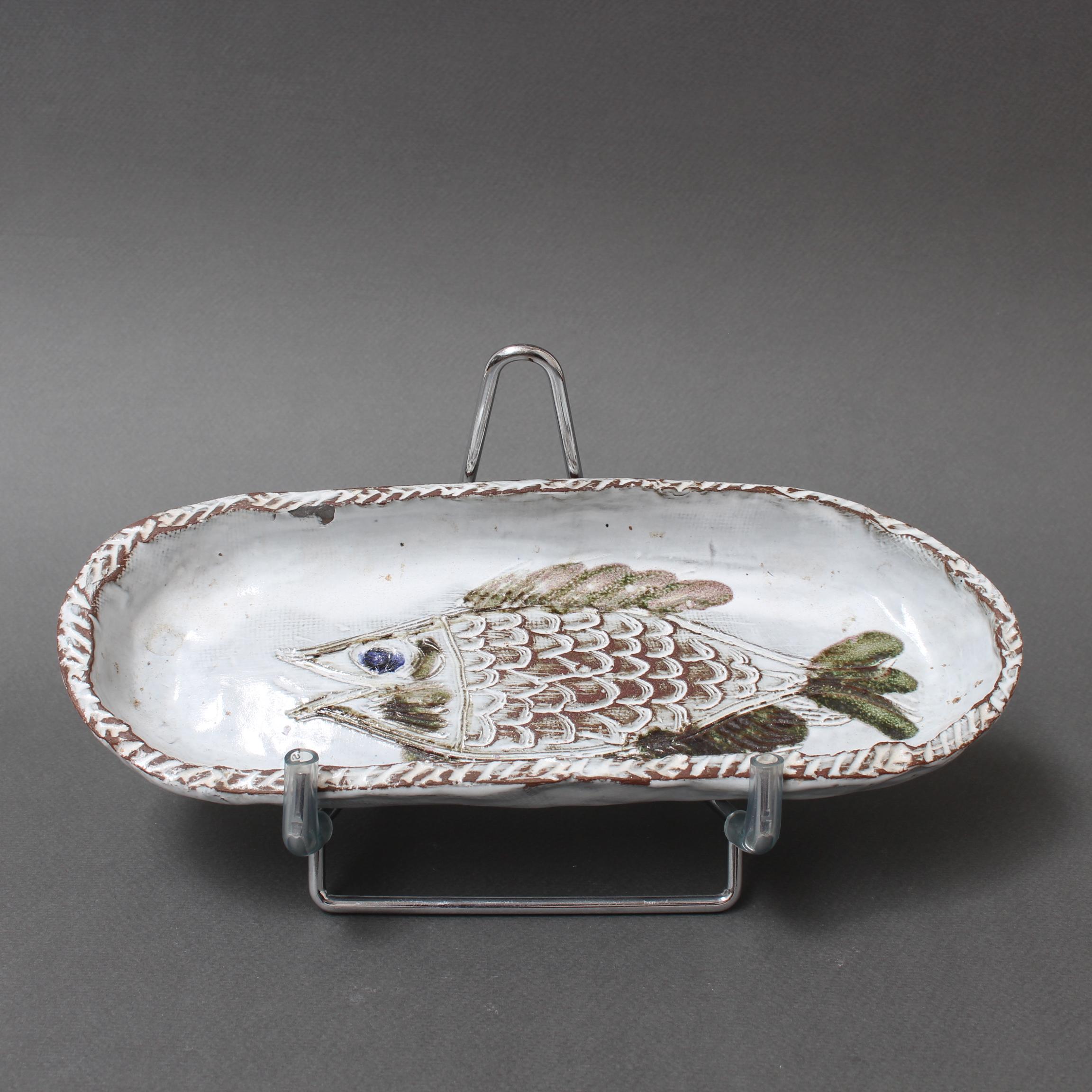 French ceramic decorative dish with fish motif (circa 1970s) by Albert Thiry. An oval-shaped ceramic dish has a chalk-white glaze surface. Within the dish's recess a fish is incised into the glaze and painted in Thiry's trademark brown, blue and