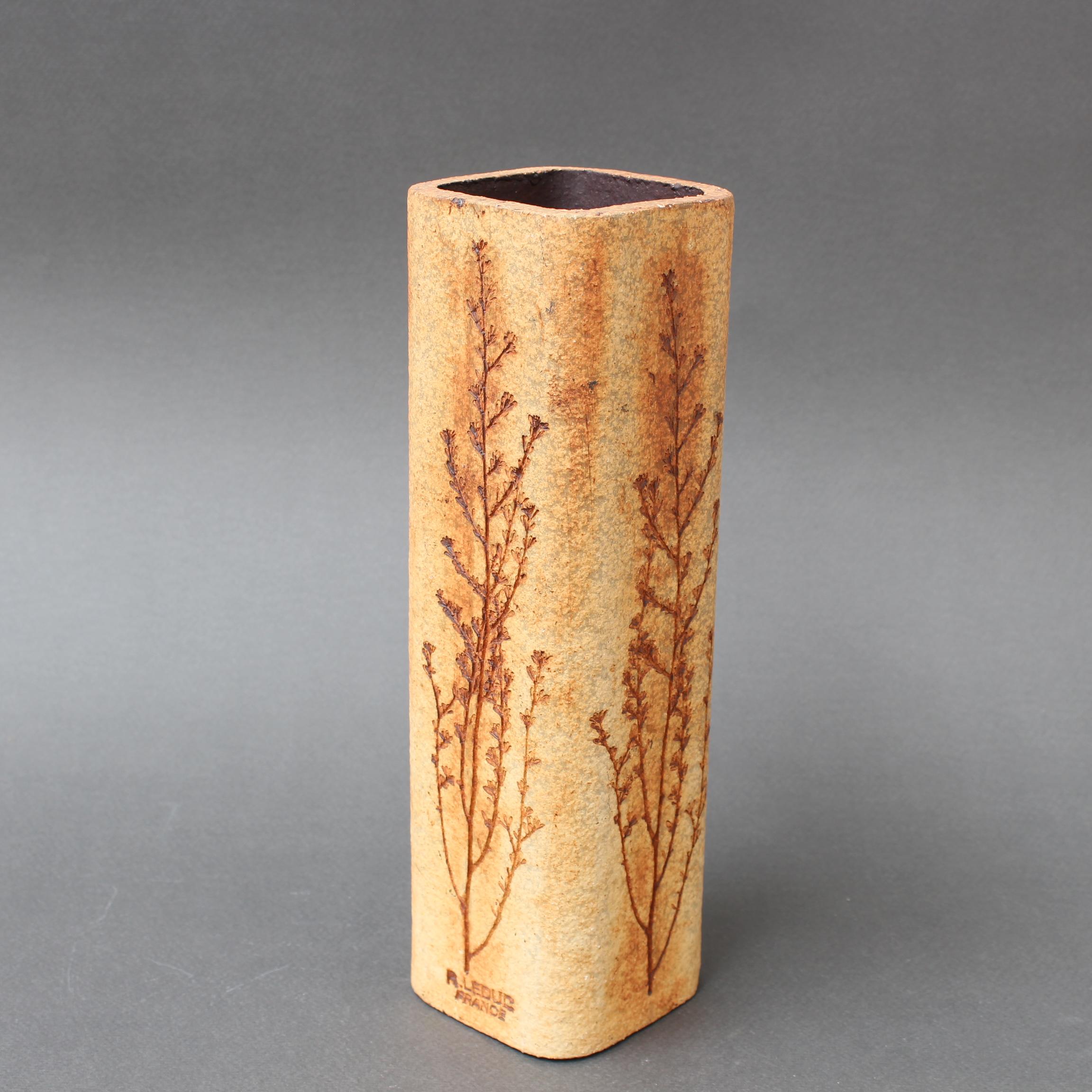 Vintage ceramic vase by Raymonde Leduc (circa 1960s). Sandstone coloured with plant motifs inlaid on all four sides. In fair overall condition showing a chip in a lower rounded corner along with some age-related marks and spotting. It has been