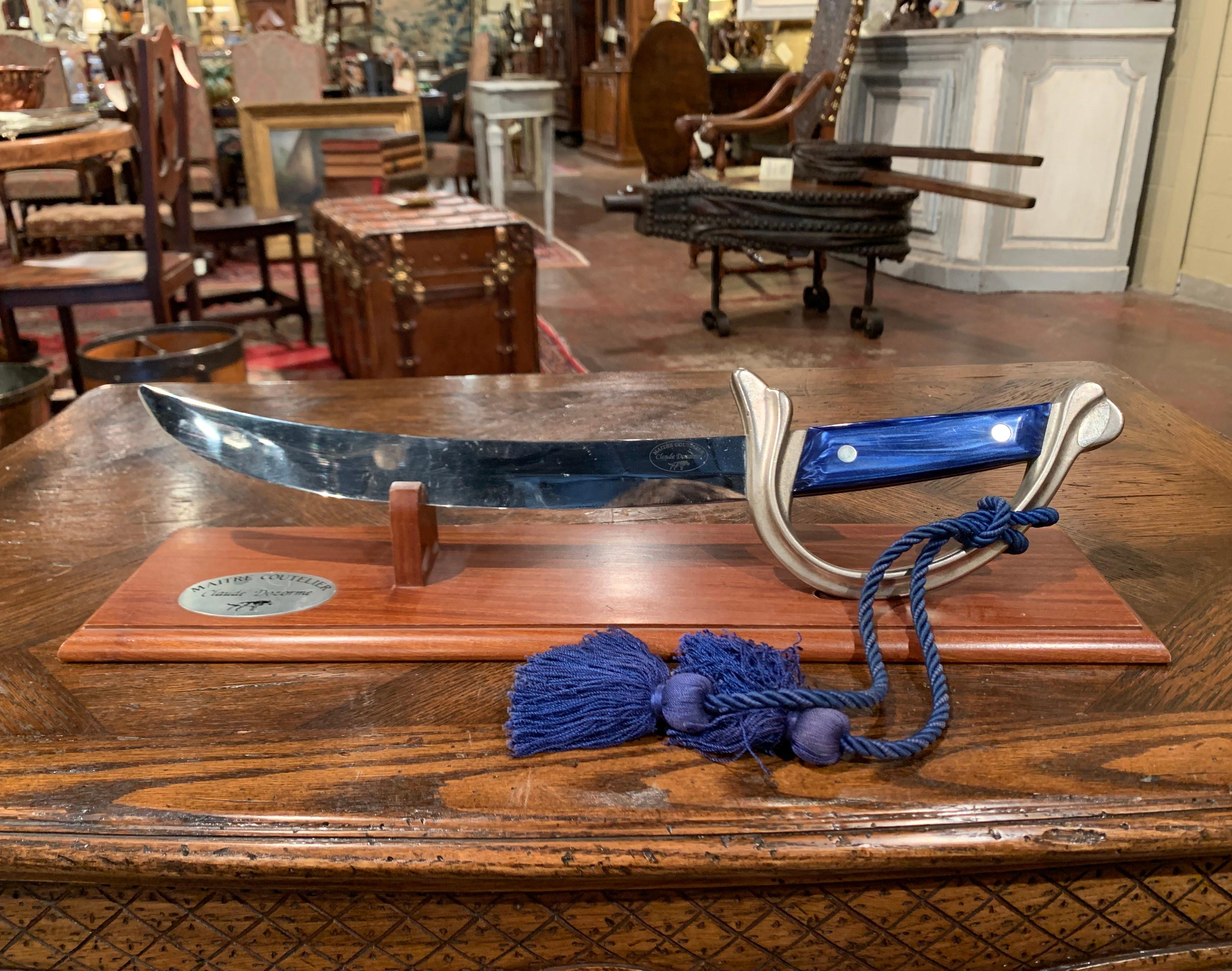This vintage metal saber with blue handle and silvered guild was created in Thiers, France circa 1970 by Claude Dozorme, maitre coutelier. The large knife rests on a walnut Stand sighed by the company. The piece is in excellent condition with a rich