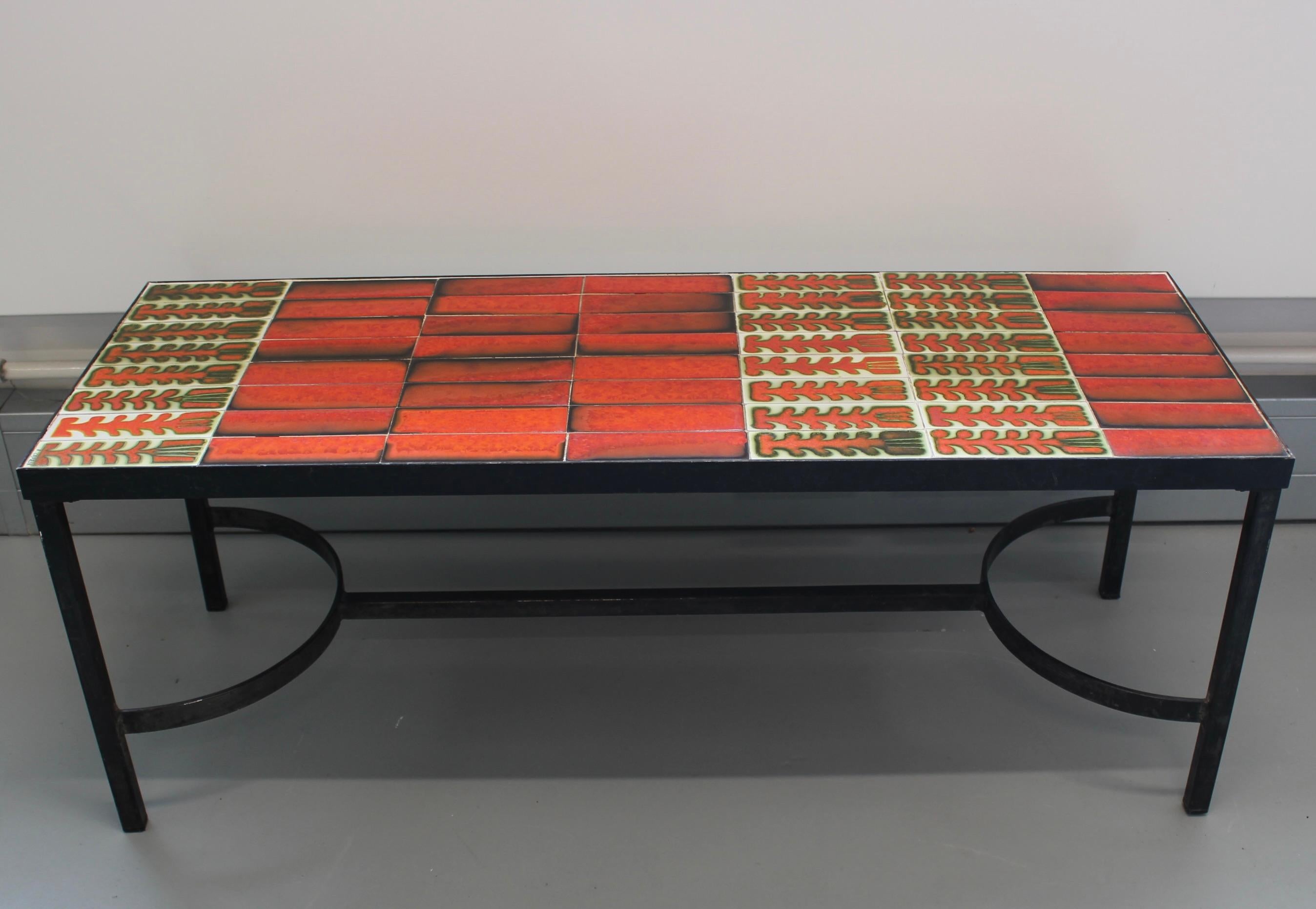 A striking example of Roger Capron’s celebrated ceramic artistry, this mid-century coffee table features a richly coloured, hand-glazed tile top in tones of red, black, and earthy green. The geometric and botanical motifs—typical of Capron’s