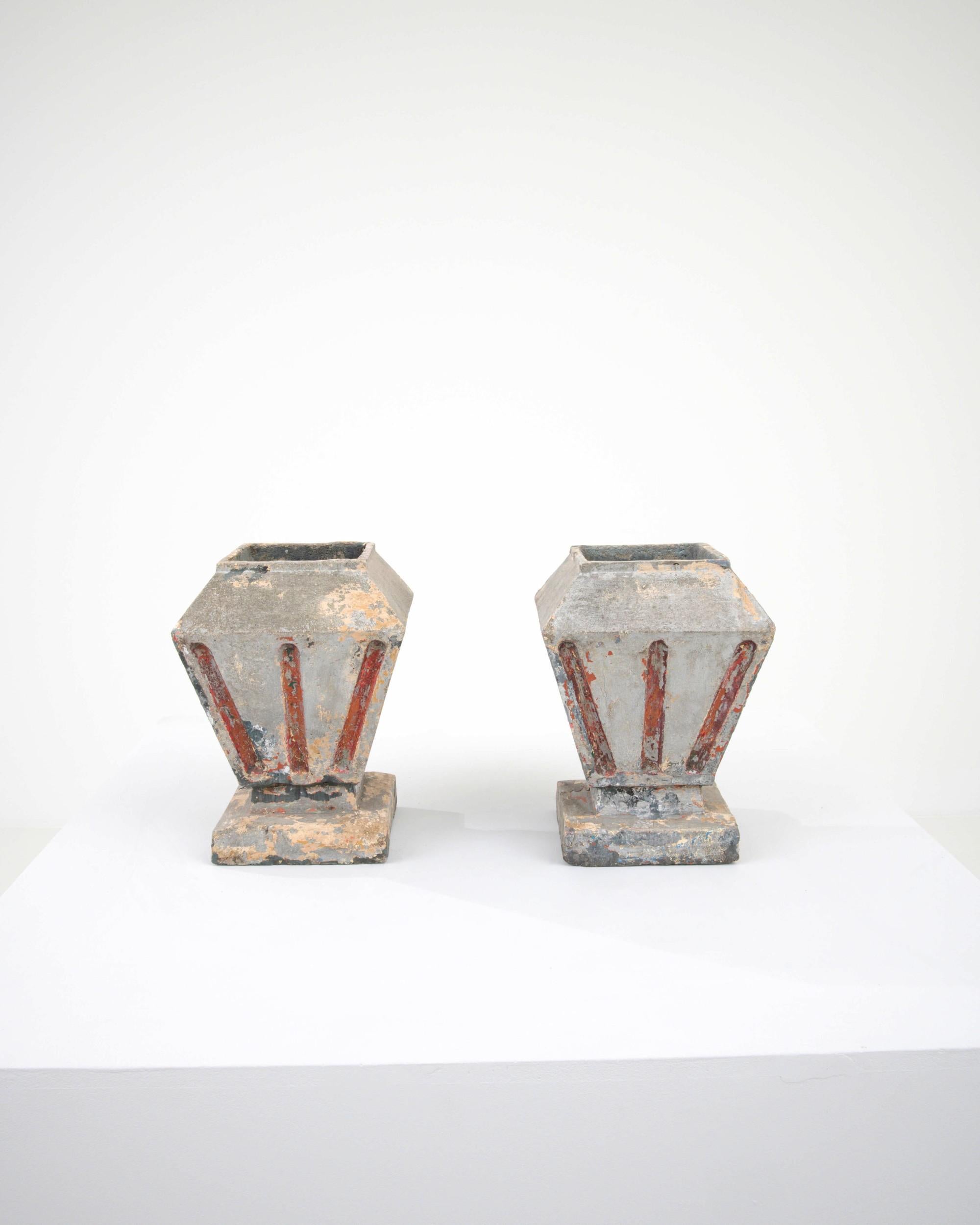 Weathered by exposure outdoors, this pair of antique urns, created in 20th century France, are brimming with unique character. A sharp geometry, artfully shaped, creates an eye-pleasing and thoughtfully provoking form. Red stripes frame the tapered