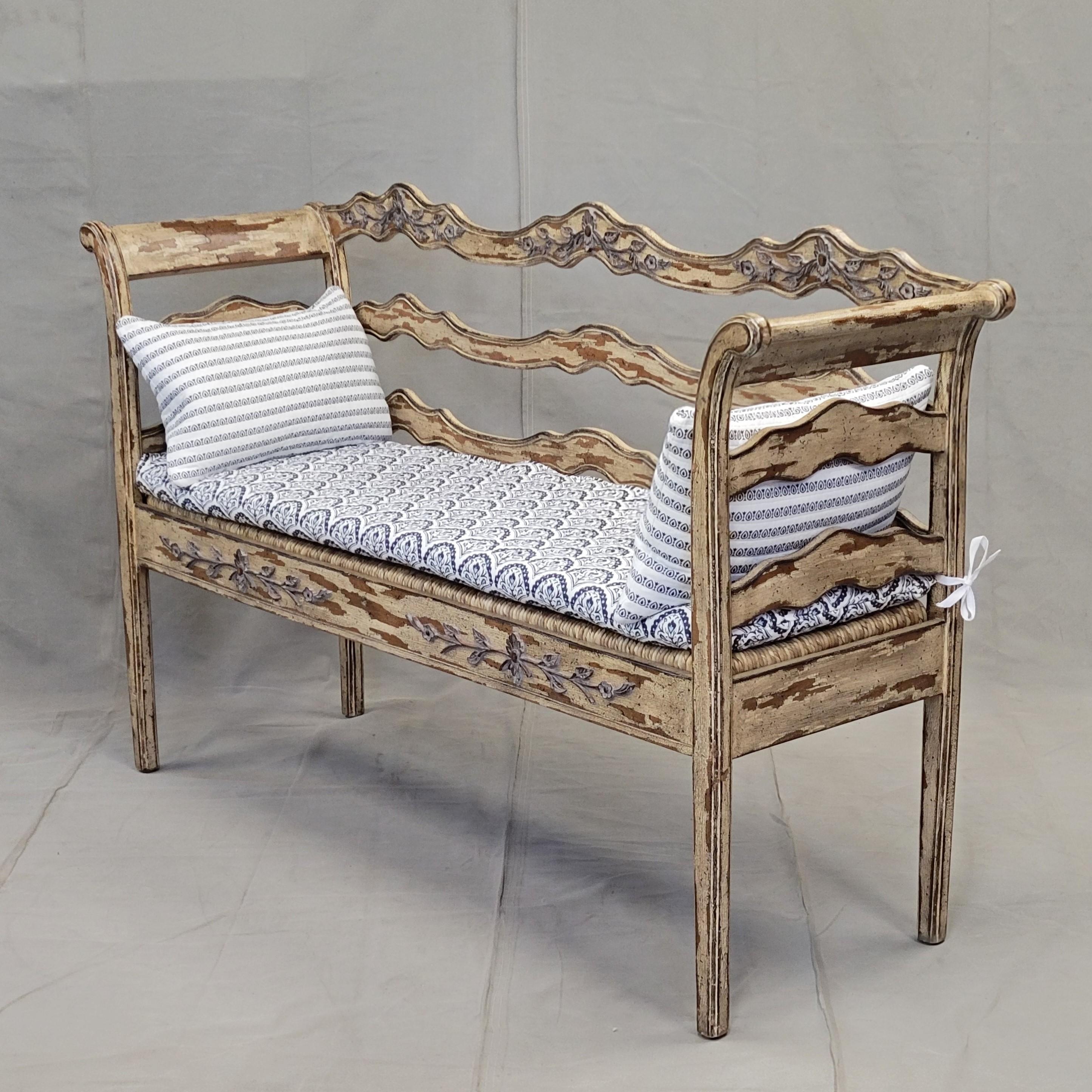 This beautiful carved wood French Country style bench has a rush seat along with a new handmade quilted cotton blue/white seat cushion and coordinating stripe down lumbar pillows. The bench backrest is adorned with hand carved floral accents. The