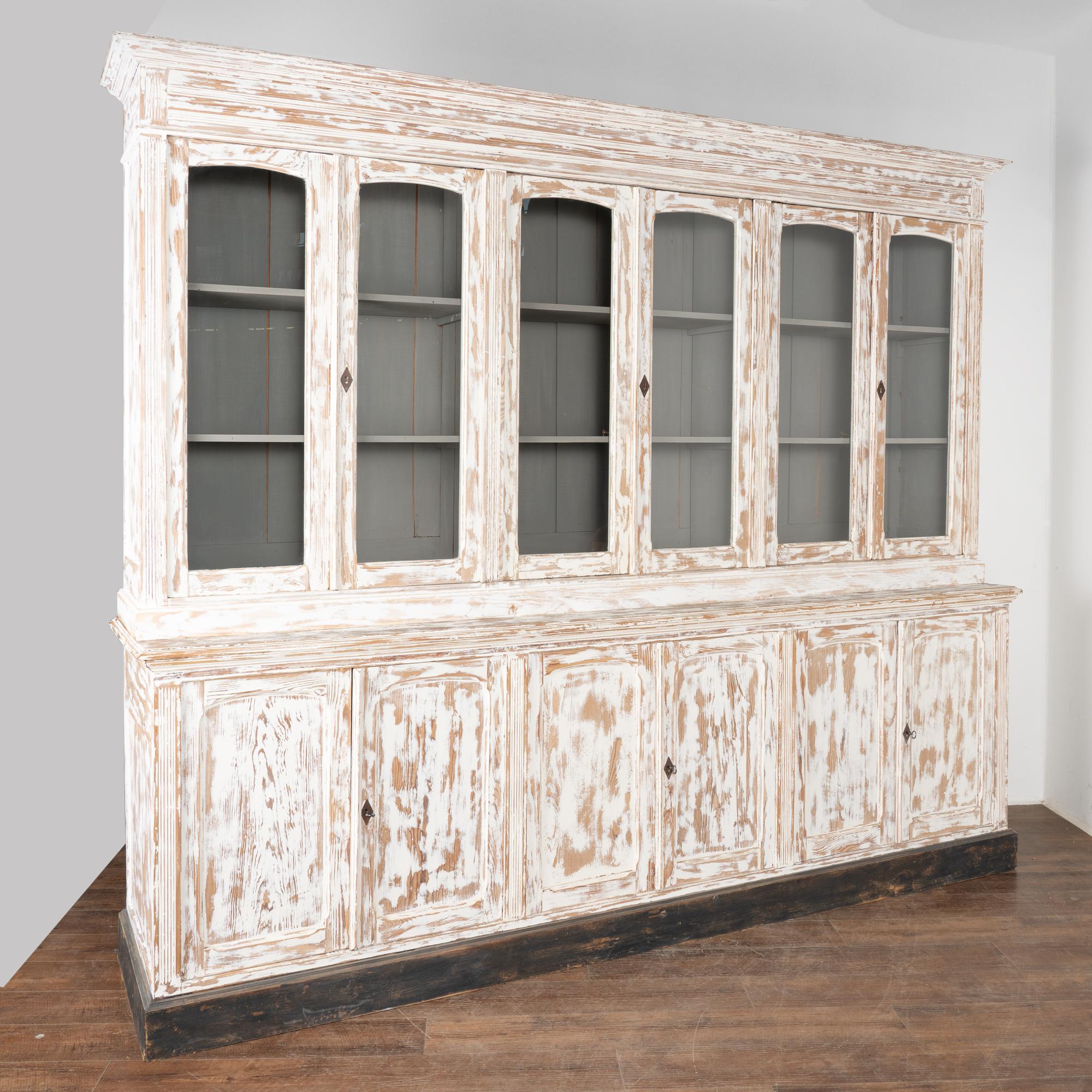 French country large display cabinet or bookcase in two sections. Six glass doors over six paneled cabinet doors.
Pine wood later painted in white, rubbed out and distressed; interior and shelving painted gray, baseboard is black.
Restored,
