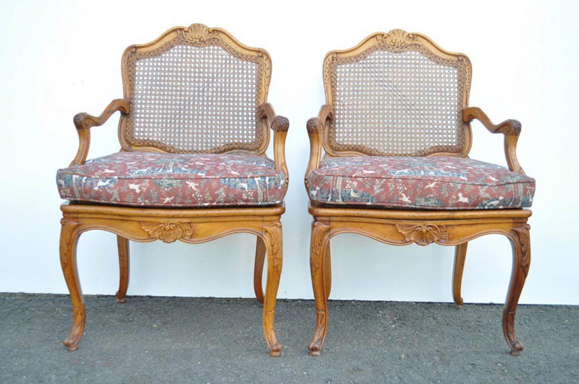 Pair of beautiful high quality vintage French Louis XV style carved caned back fauteuil armchairs. The chairs feature richly carved cabriole legs, scrollwork arms, and shell and acanthus accents. The seat cushions are a woven fabric with trees,