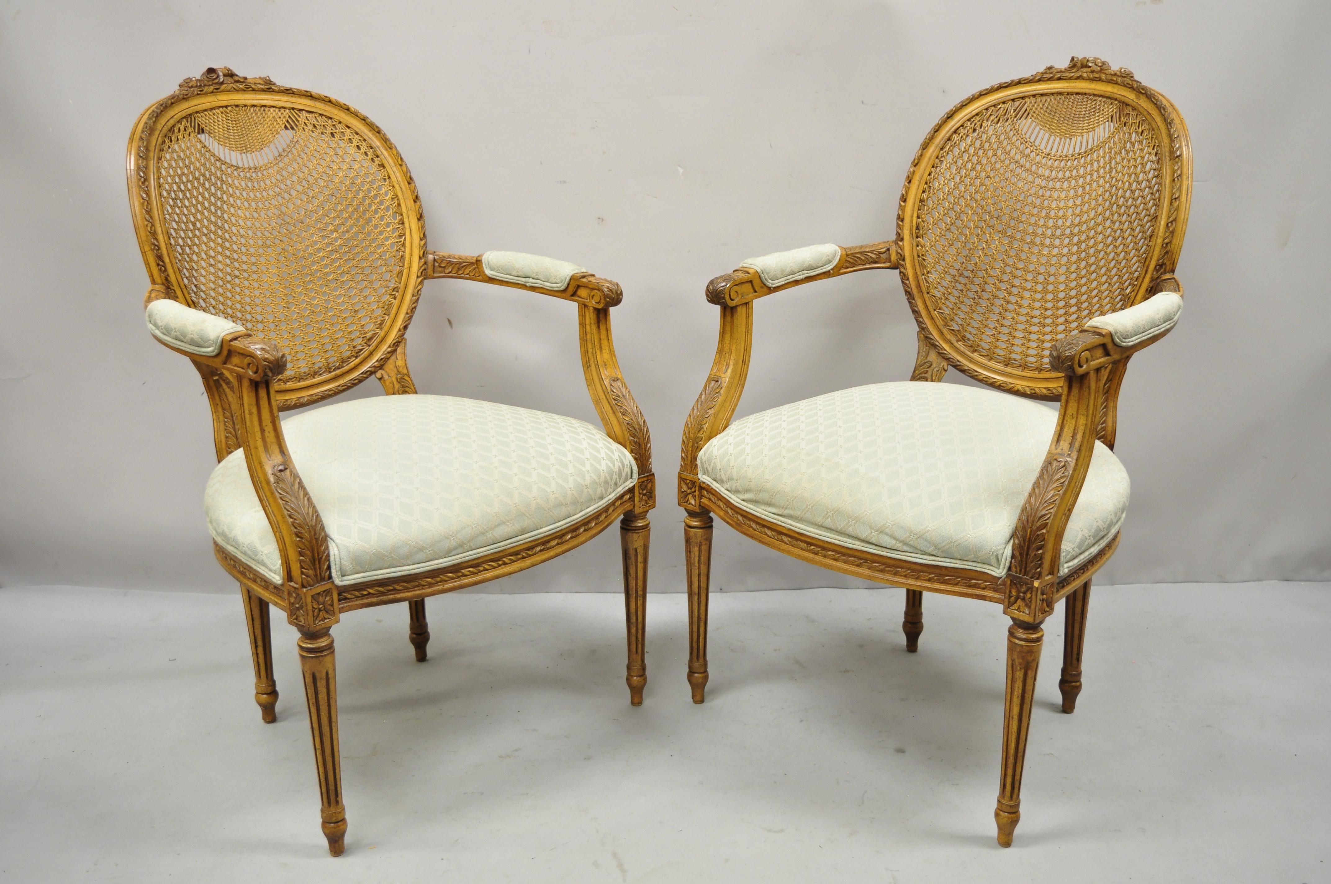 Vintage French Country Louis XVI oval cane back fauteuil lounge arm chairs - a pair. Item features cane backs with ornate weave to top of backs, solid wood frames, beautiful wood grain, upholstered arm rests, distressed finish, tapered legs, very