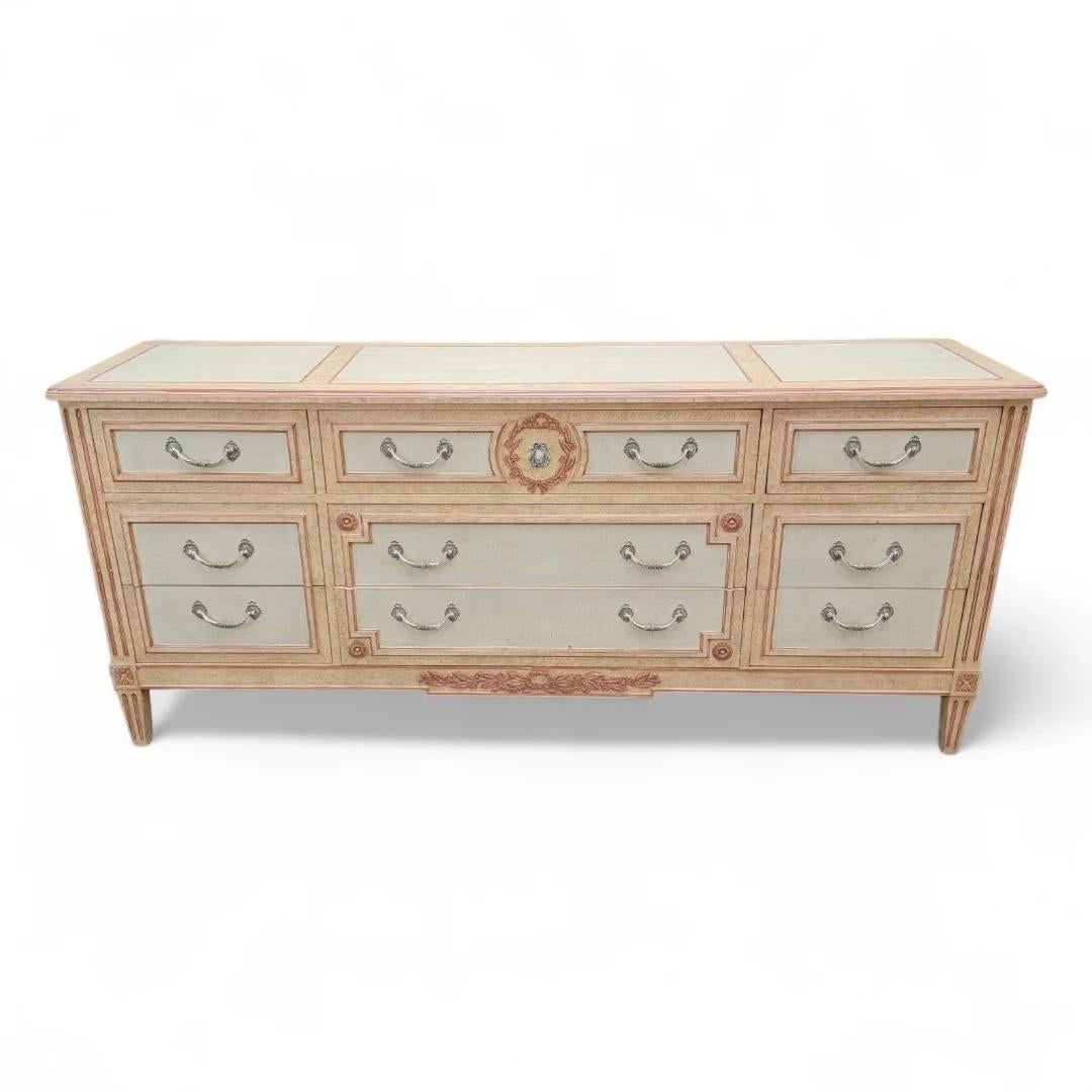 Vintage French Country Style Hand Painted 9 Drawer Dresser by Baker Furniture Co.

A gorgeous French Country/Regency Louis XVI/Swedish Gustavian style dresser by Baker Furniture USA. Carved, cream painted walnut, with peachy pink trim and accents