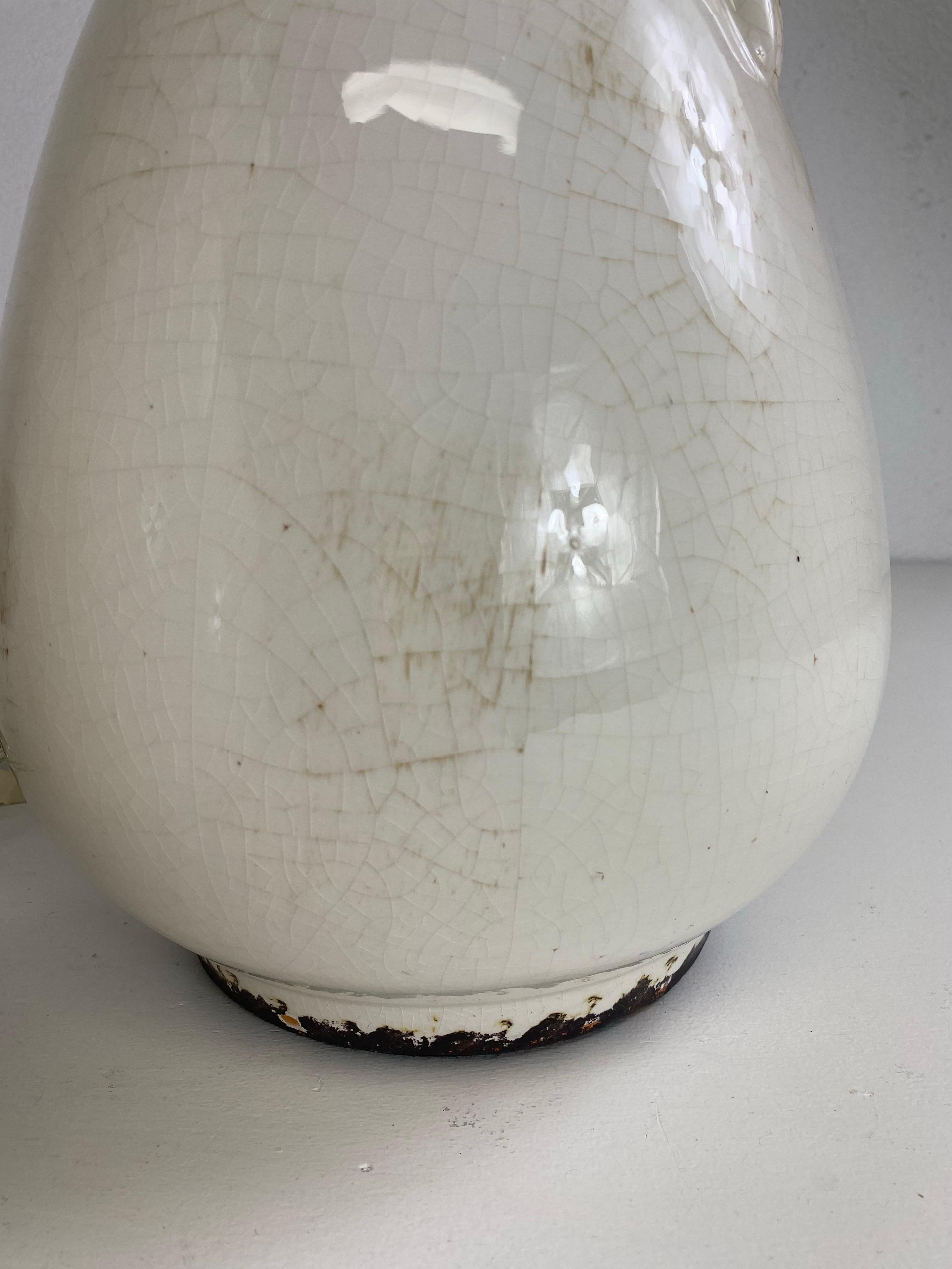 This is a vintage pair of French country inspired rustic pottery table lamps. This pair of table lamps have a cream colored crackled antiqued glazed the surface with swirl handles on either side. These lamps are in working order and feature their