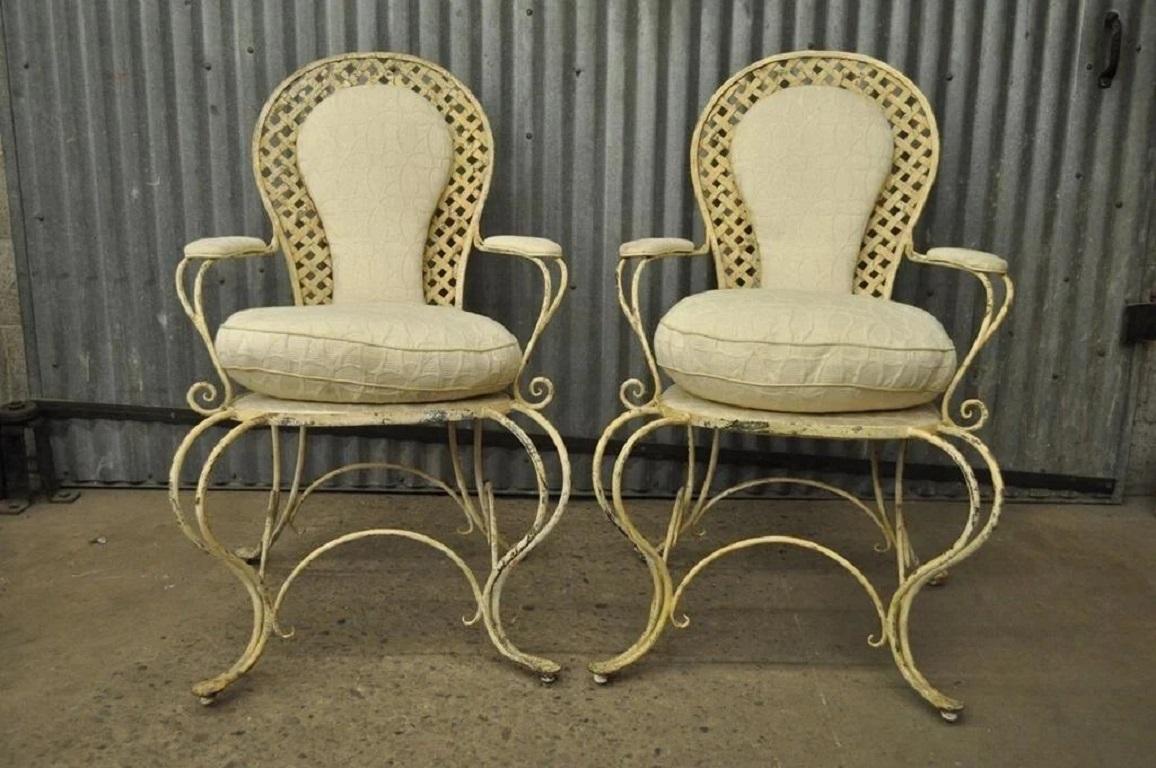 Vintage French Country Wrought Iron Lattice Scrolling Arm Chairs (A) - Pair. Item features sturdy iron construction, shapely whimsical frames, curule form arms and legs, distress painted finish, down seat cushions, and ball bearing rolling casters.