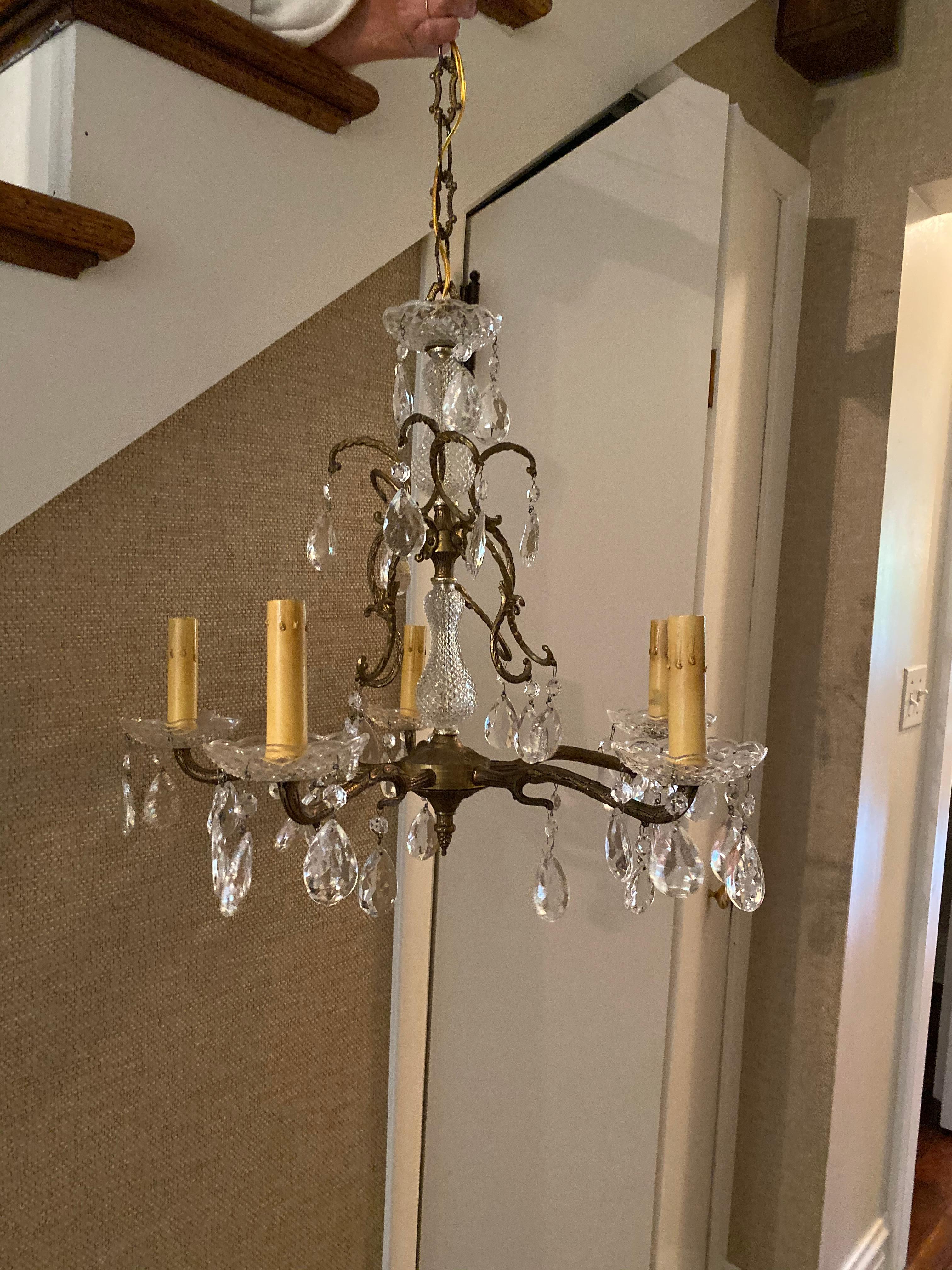 On holiday in Paris, we found this petite and charming 5-armed chandelier at the Marche Aux Puces.
The stunning crystal chandelier has hand forged bronze frame, glass cups around candles and dripping crystals. Perfect in a powder room, hallway,