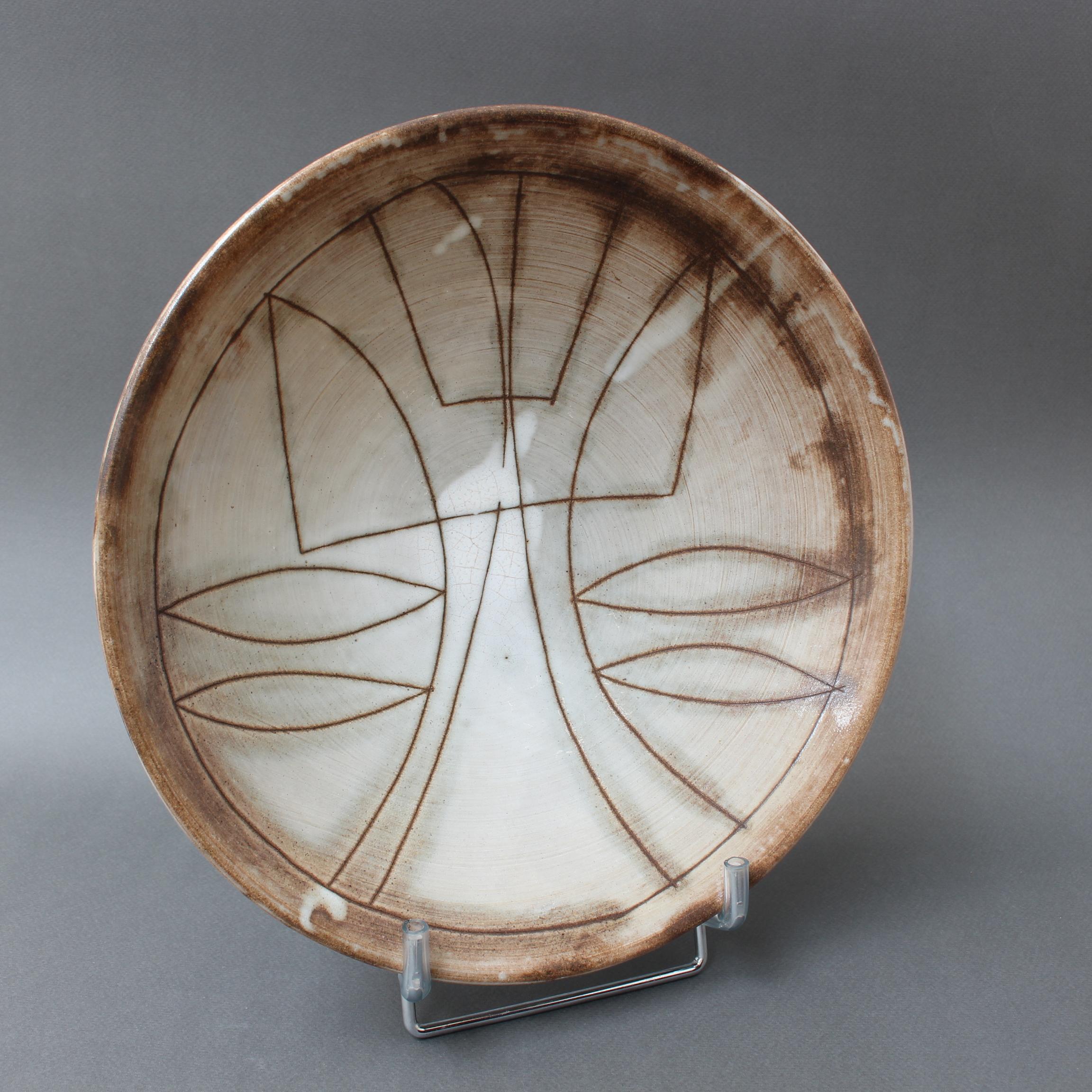 Mid-century decorative bowl (circa 1960s) by Jacques Pouchain - Atelier Dieulefit. This elegant bowl, elevated by a small circular base, was created in Pouchain's trademark tones and glaze. The bowl's recess is decorated with a stylised flower in