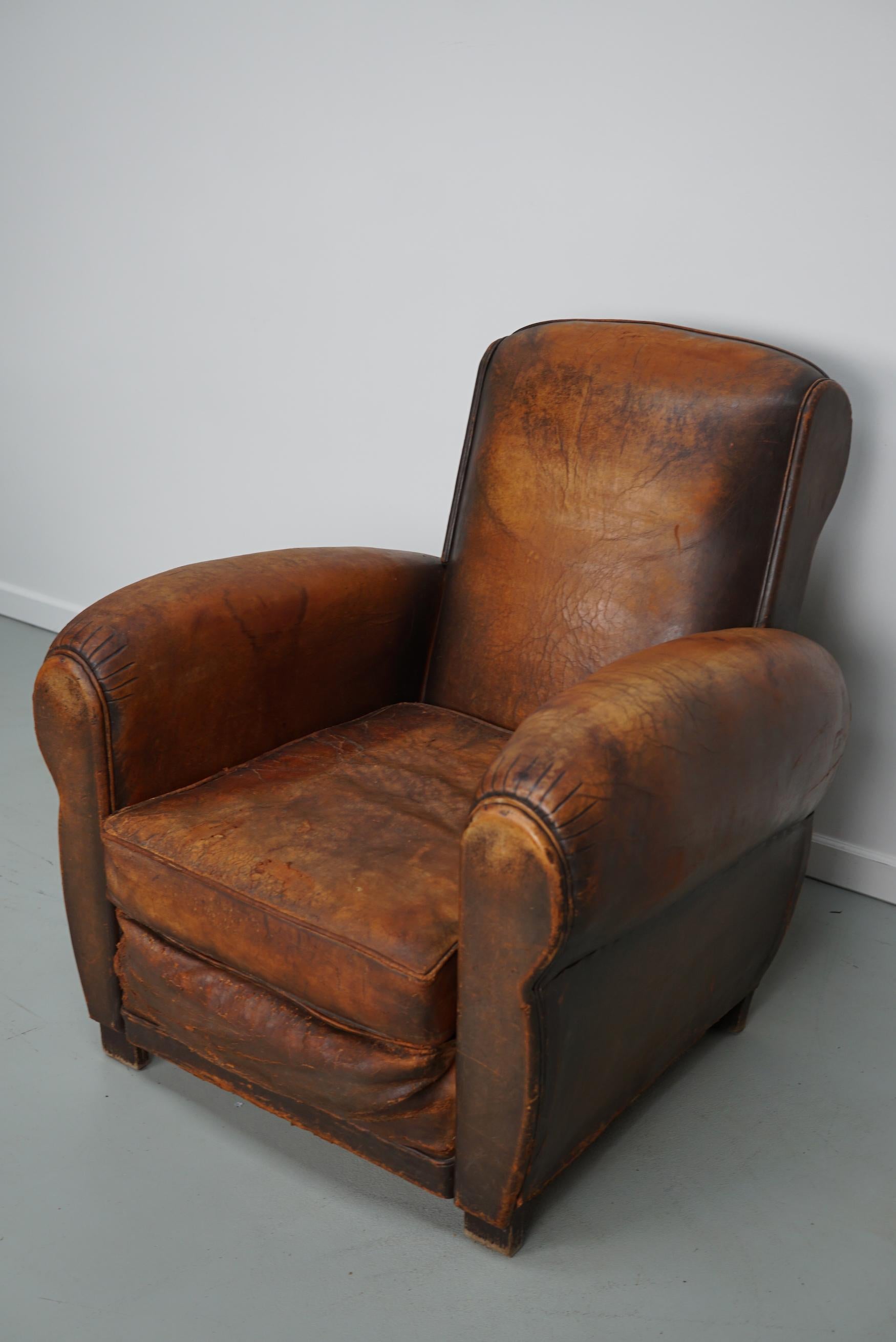 This cognac-colored leather club chair comes from France. It is upholstered with cognac-colored leather and features metal rivets and wooden legs. The springs have been replaced by modern foam so the seat is in good condition.