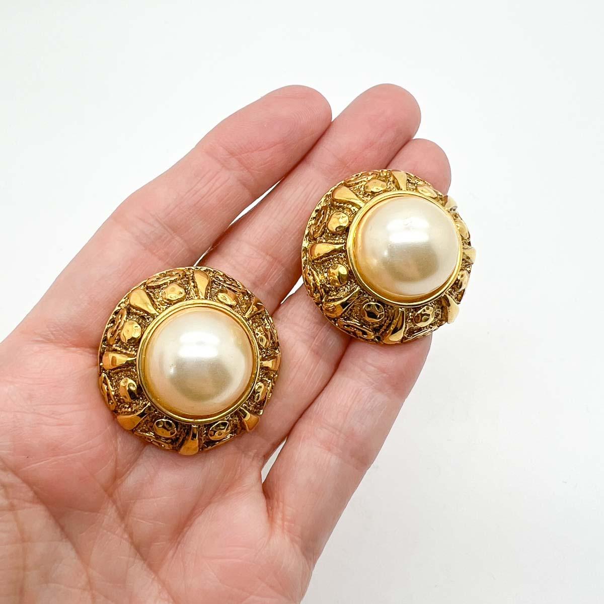 A wonderful pair of French couture vintage Etruscan pearl earrings dating to the 1980s. A stunning embossed gallery frames the large lustrous half pearls. Quintessentially 80s and forever chic. Owing to the construction, pattern, and design these