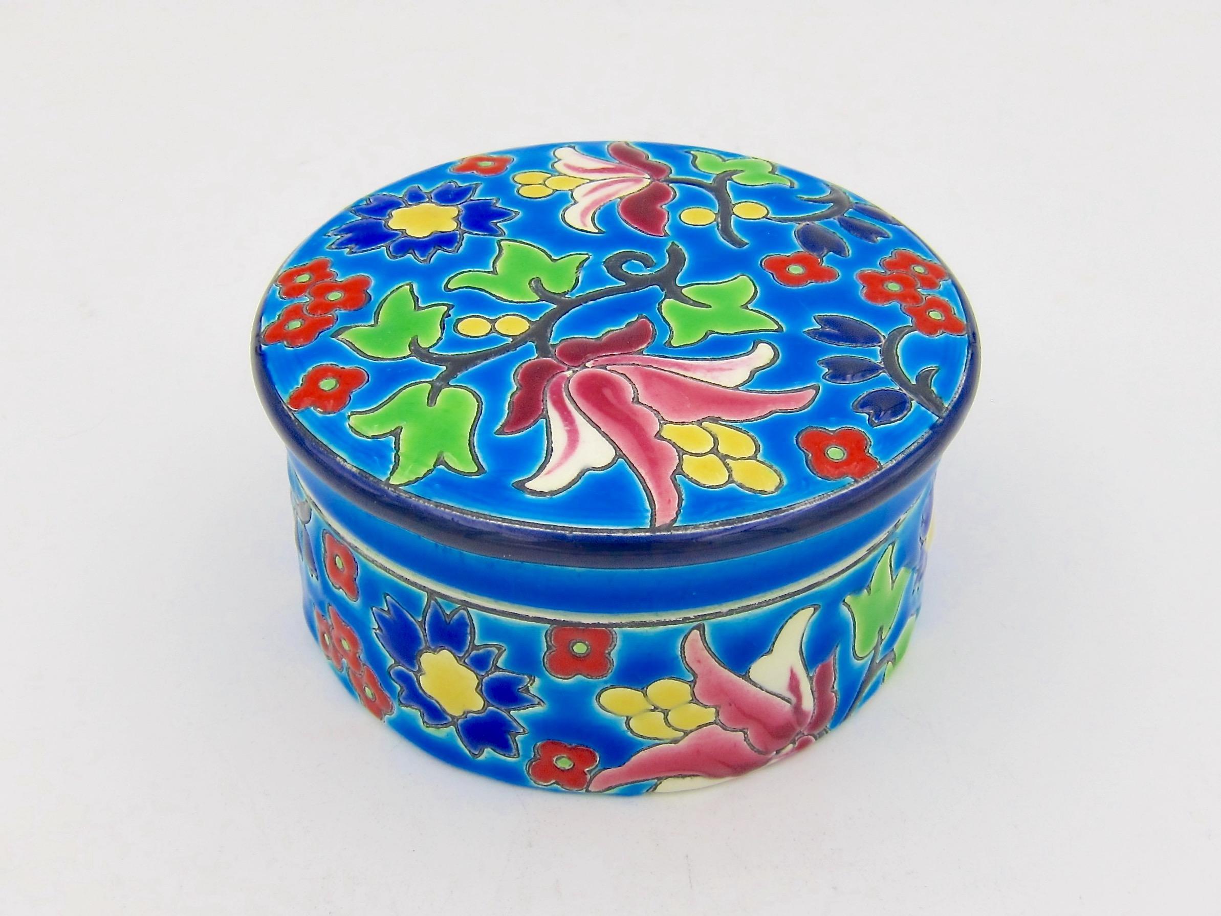 A vintage French faience keepsake, trinket, or vanity box from the Emaux de Longwy art pottery workshop of France. The ceramic box is hand-decorated with a bold and colorful Chinoiserie style glaze of multi-colored blossoms, green leaves, and black