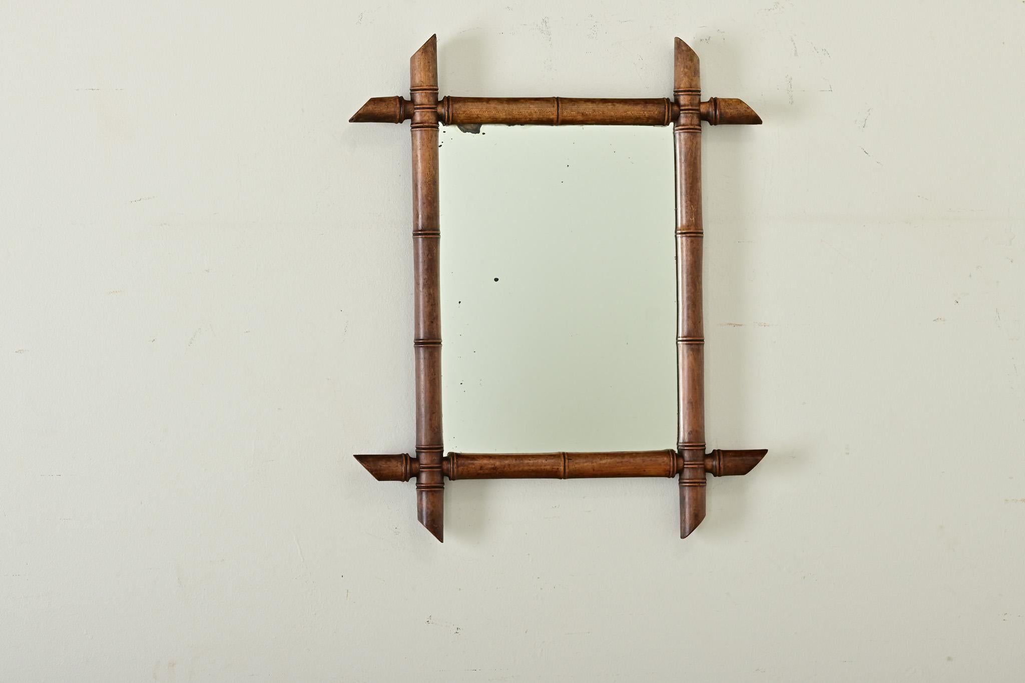 A delightful vintage faux-bamboo pine mirror from the 20th century, with a lovely honey brown patina. This rustic mirror features a rectangular silhouette made of a carved faux bamboo frame showing slanted corners. This mirror charms us with its