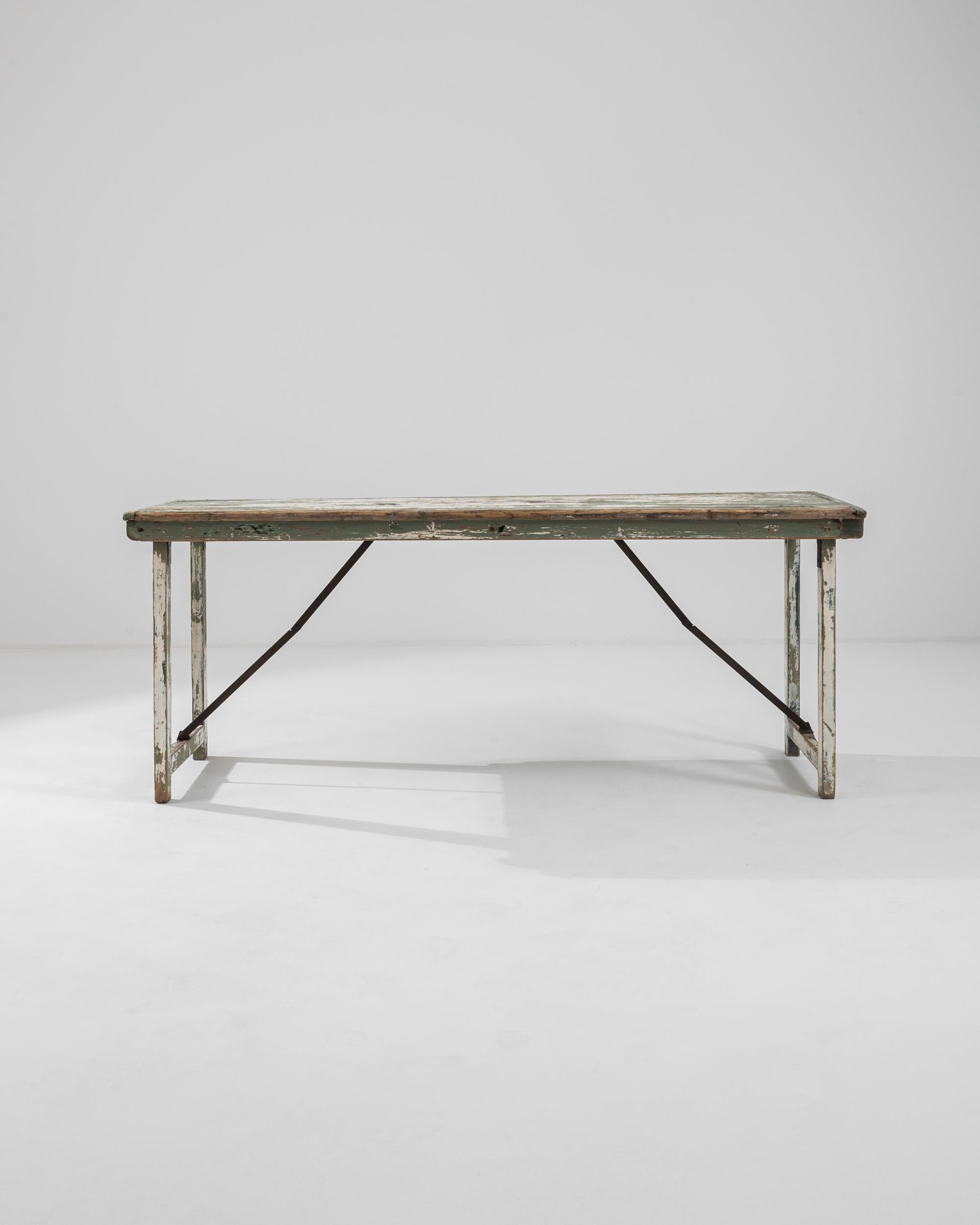 A wooden and metal dining table created in 20th century France. With a simple yet eye-pleasing design, and a delightfully colored surface, this expansive table easily unfolds for an aesthetically pleasing picnic. The green paint that coats its