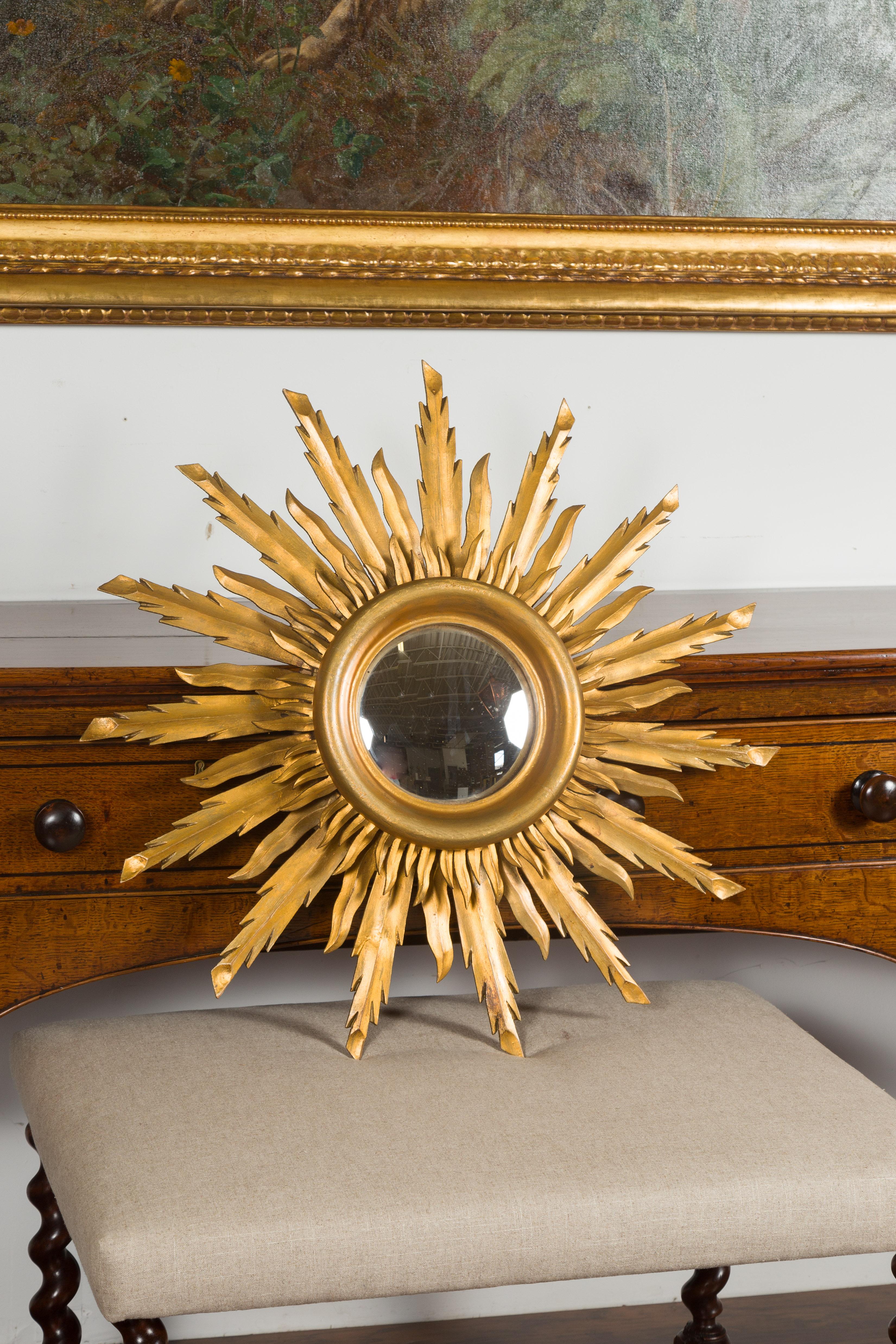 A French vintage giltwood sunburst convex mirror from the mid-20th century, with rays of varying heights. Created in France during the midcentury period, this sunburst mirror charms us with its graceful lines and golden finish. Surrounding a central