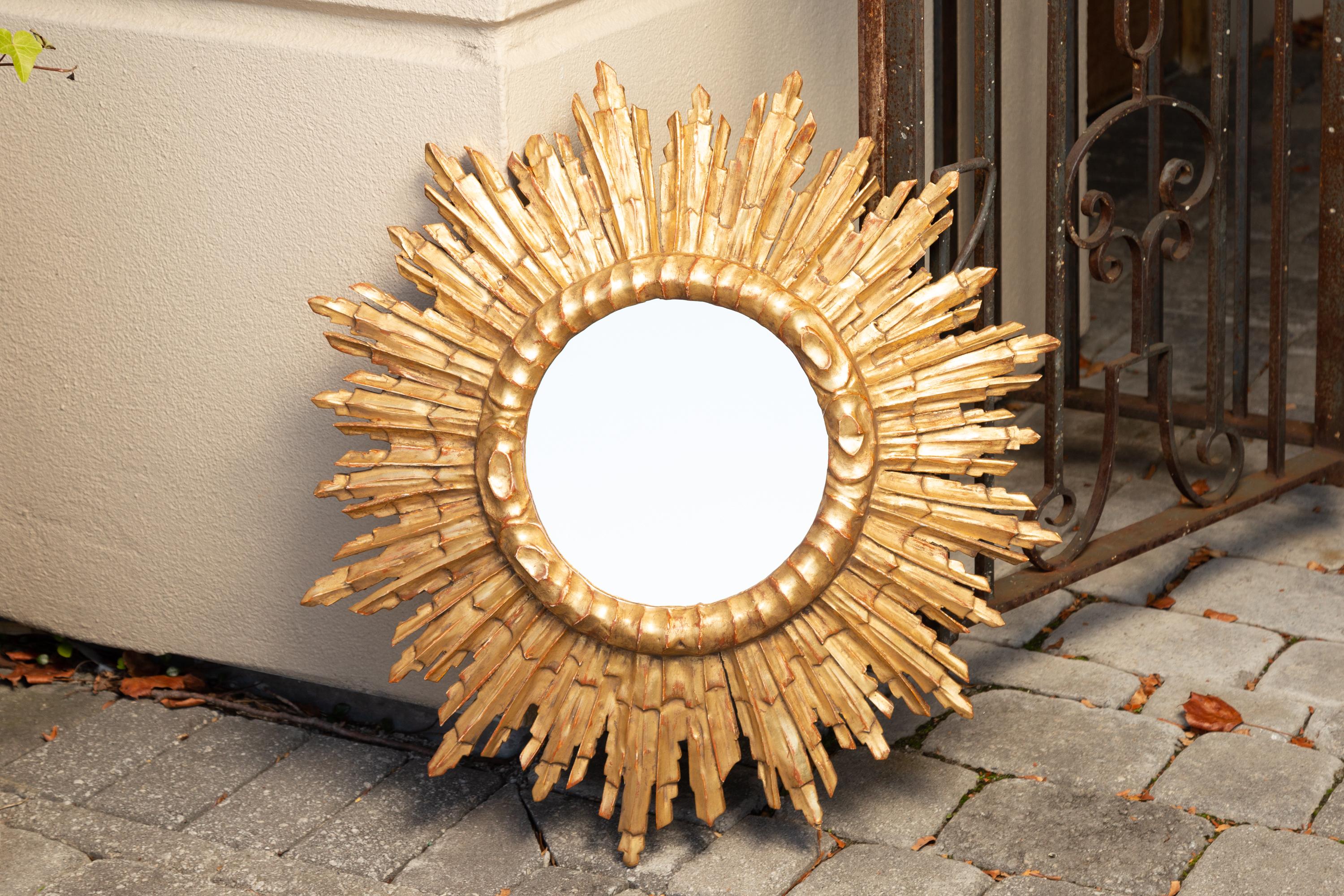A French vintage giltwood sunburst mirror from the mid-20th century, with rays of varying sizes and cloudy frame. Born in France during the midcentury period, this exquisite sunburst mirror features a circular mirror plate surrounded by a cloudy