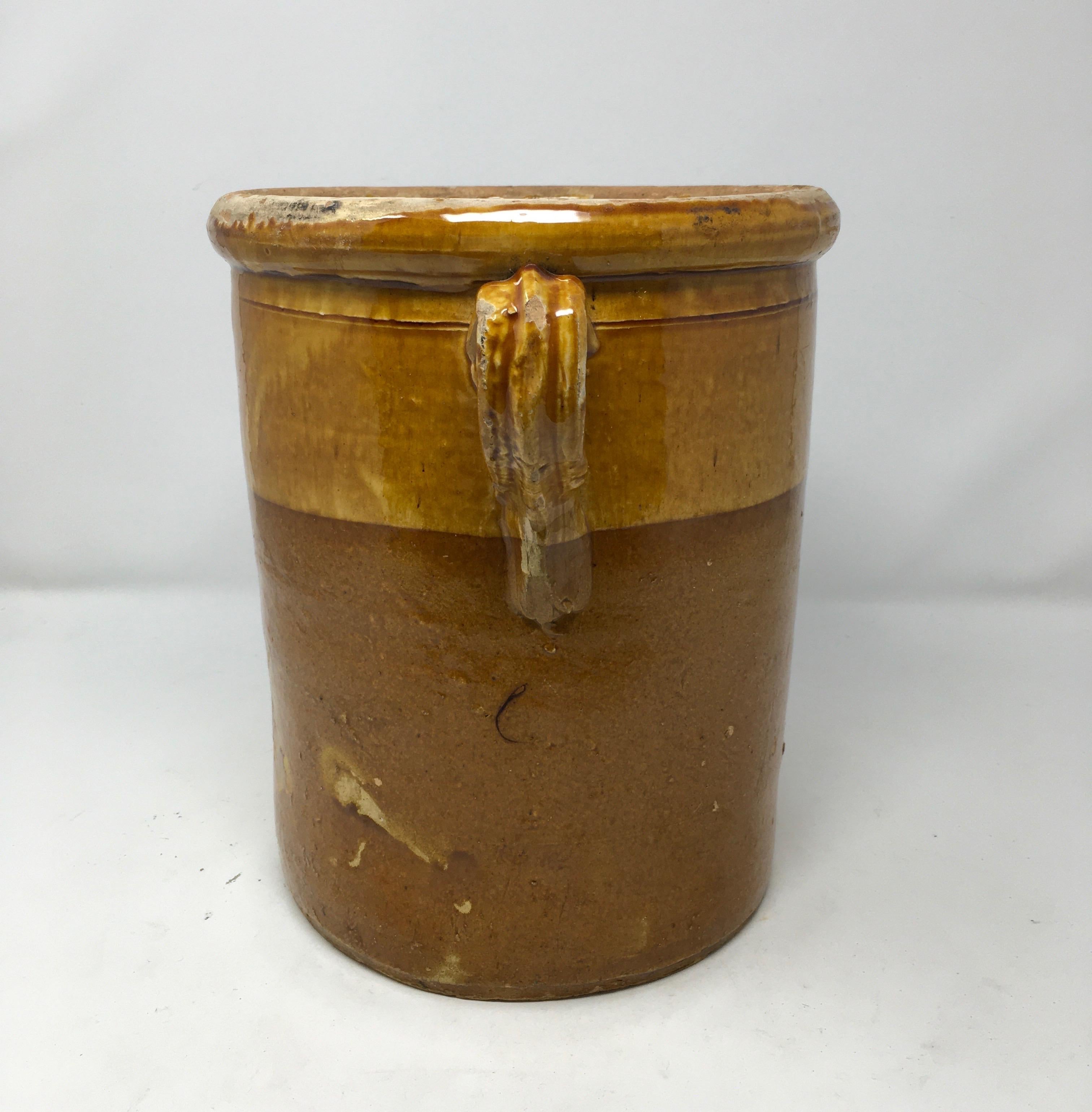 We found this glazed earthenware crock in Southern France. The top half of this large stoneware crock has a shiny mustard yellow colored glaze with a brown glaze on the lower portion. This piece is in good condition with some minor ware around the