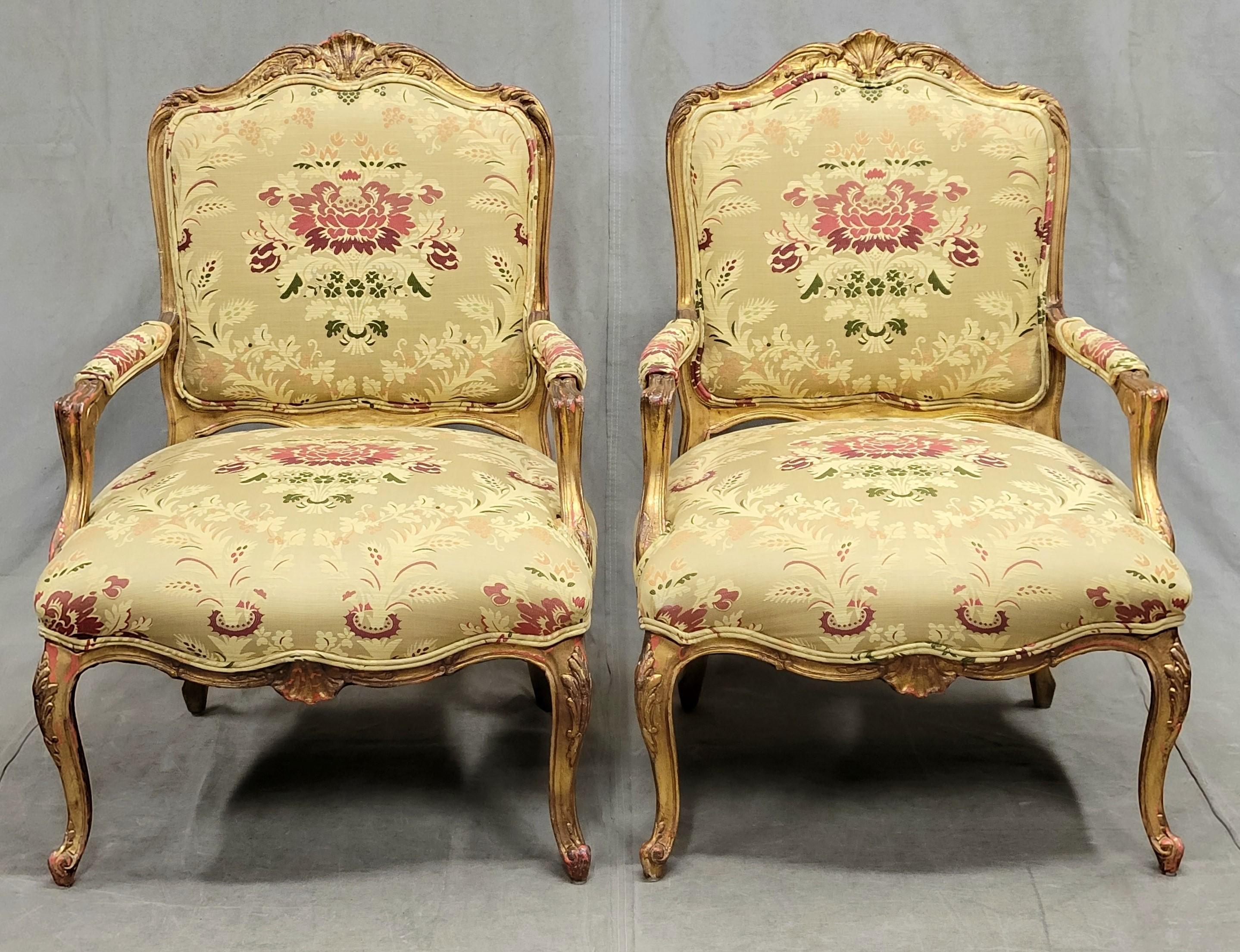 An opulent pair of French bergere chairs with gold leaf wood frames and new designer damask upholstery in shades of pale gold, cranberry red, and moss green. Seats are tight and chair frames are strong. The pair create an elegant seating area and