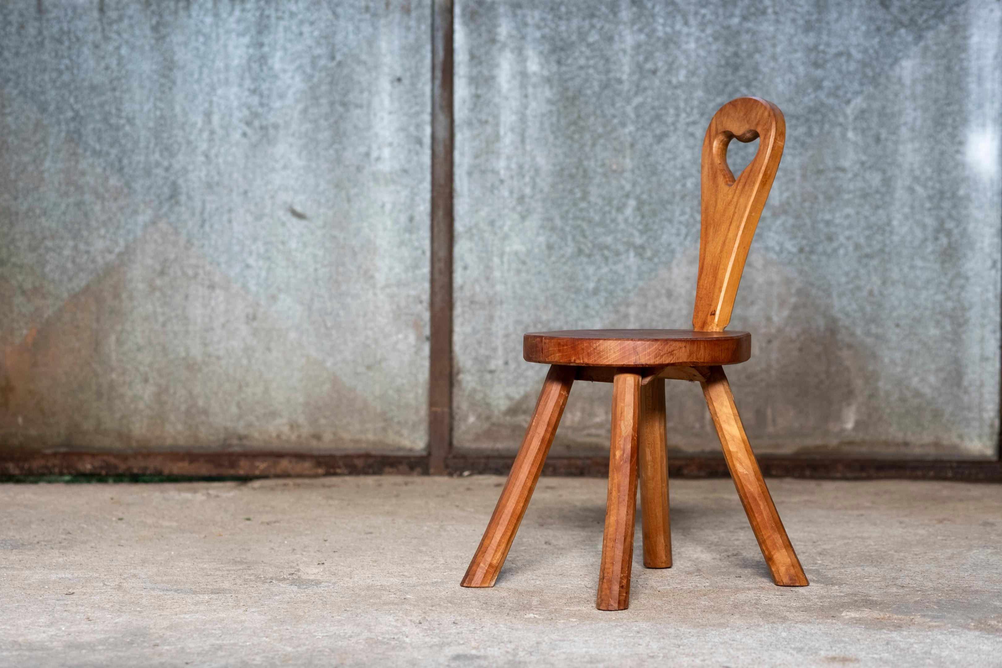 Ce charmant tabouret sculpté à la main, fabriqué en France dans les années 1970, est un délicieux mélange d'artisanat rustique et de design ludique. Fabriqué en bois massif, le tabouret présente un dossier distinctif avec une découpe en forme de
