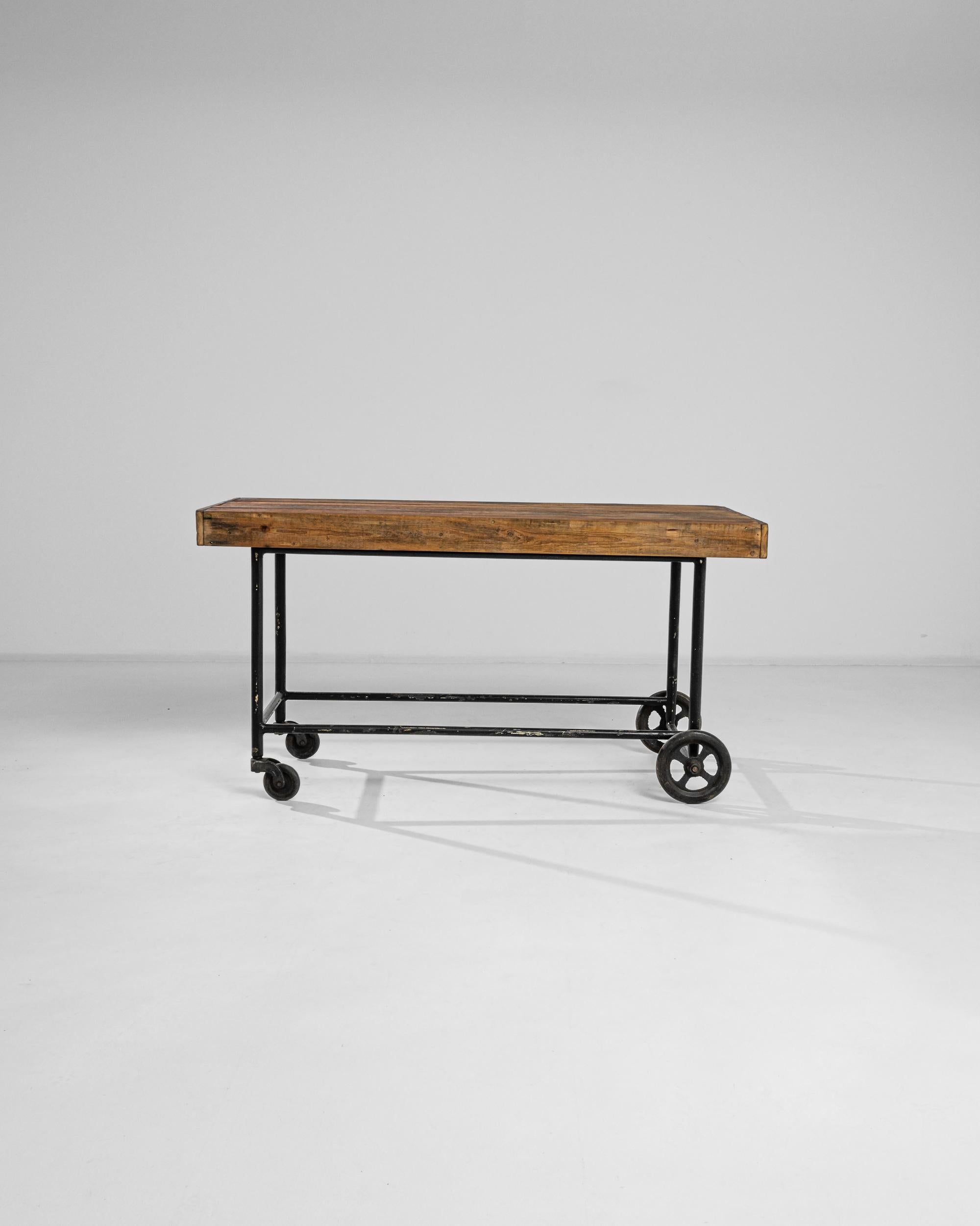 A 20th century metal and wooden table from France, sporting a sturdy top made of assembled boards, metal wheels and a black metal frame with a distinctive patina. Simple yet elegant, the practical design fits any corner, moving to adapt the needs of