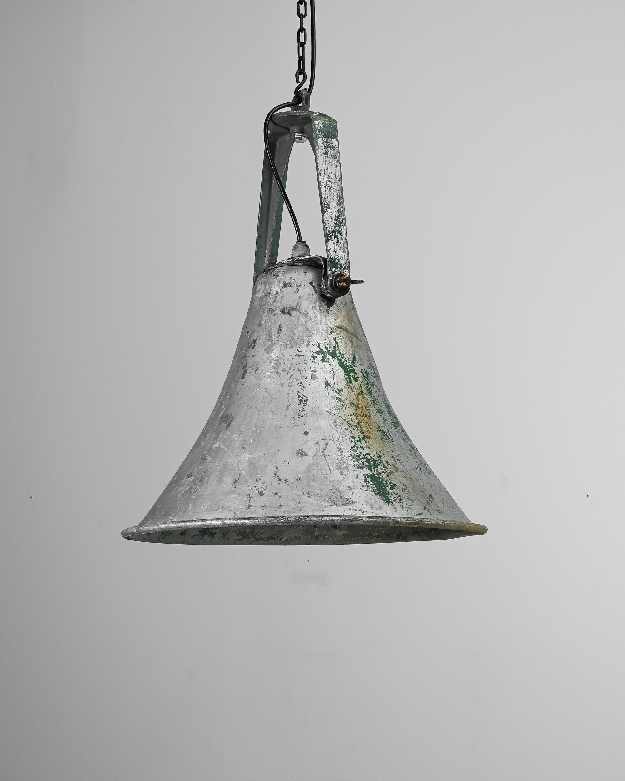 A 20th Century metal lamp from France. Hanging on a chain, the stripped-down metal shade exhibits a patinated interior and a flared silhouette, creating a diffuse light for a warm atmosphere. The bottle green specks lend the piece a rustic elegance,