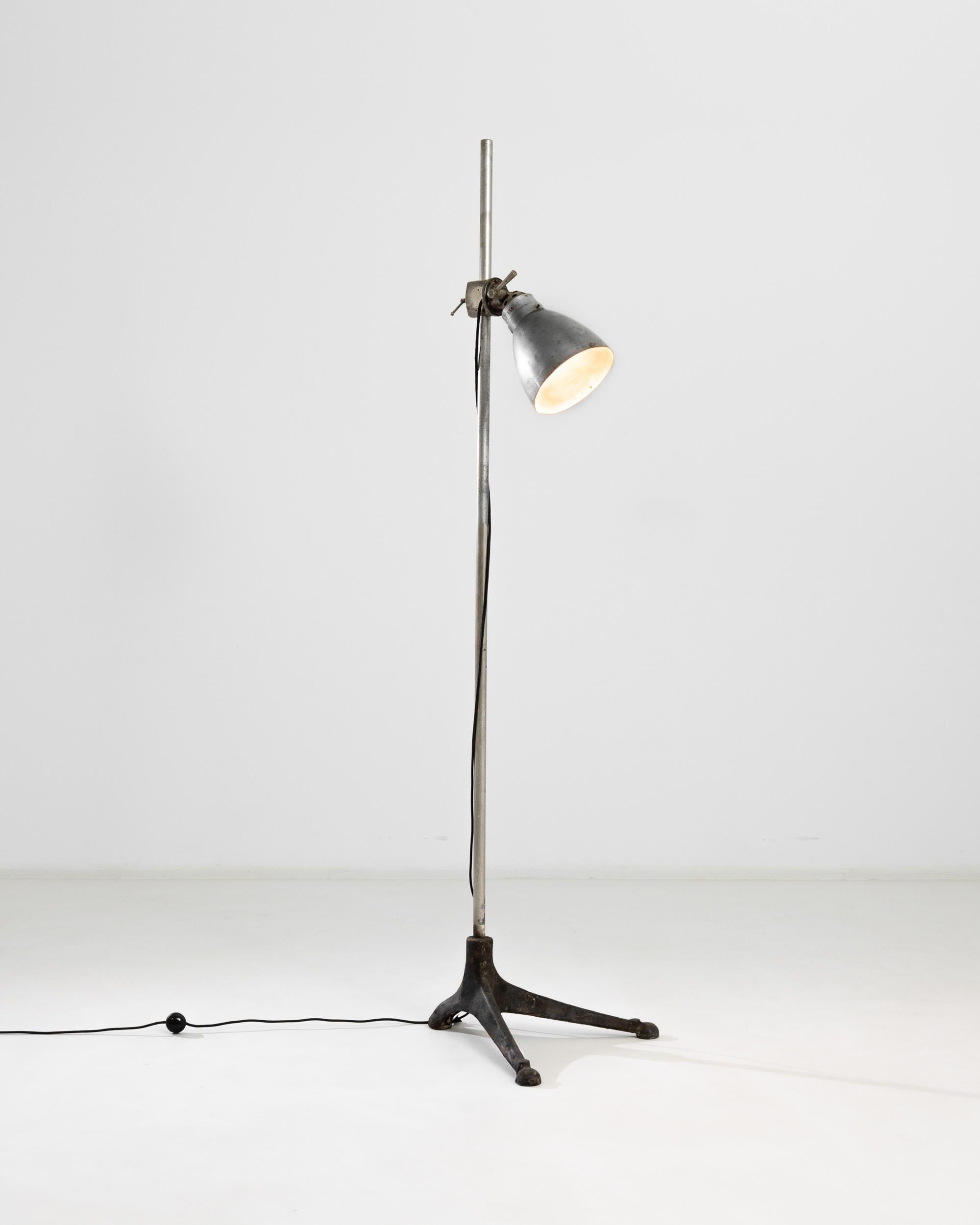A 20th century metal floor lamp produced in France, this vintage piece features an adjustable shade and irregular wrought iron tripod feet, lending the lamp a peculiar profile. The tall pole elevates above eighty inches, giving the lamp a wide range