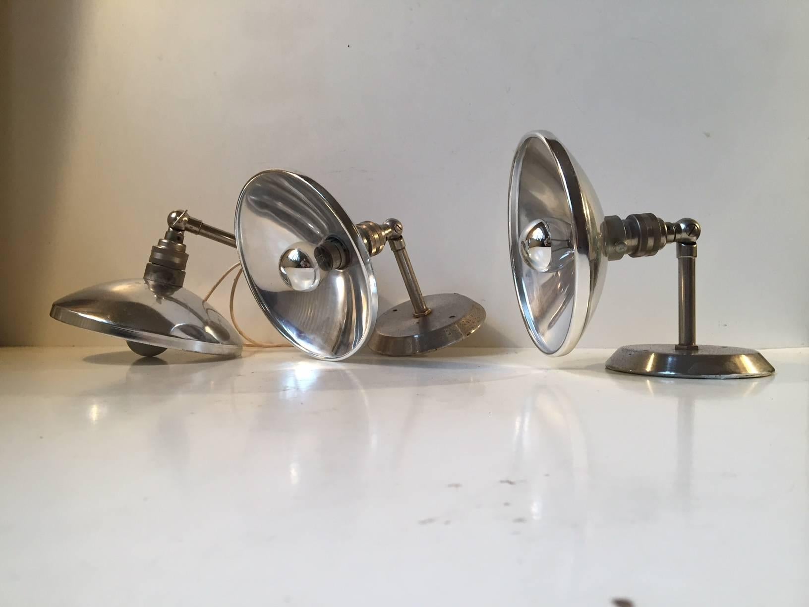 This set of three French wall lights features engine turned stems and aluminum reflectors. This set was sourced from an old warehouse. The style is reminiscent of Jielde and Bauhaus fixtures. They are fitted with their original Bayonet socket.