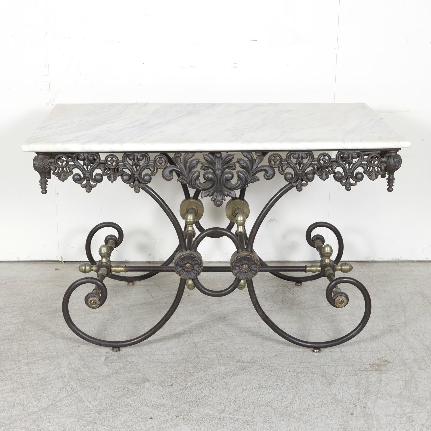 A vintage French patisserie or pastry table, circa 1940s, having a solid rectangular Carrara marble top above a wrought iron apron featuring attractive pierced foliate and stylized fleur de lis details. Supported on a scrolling iron frame joined by