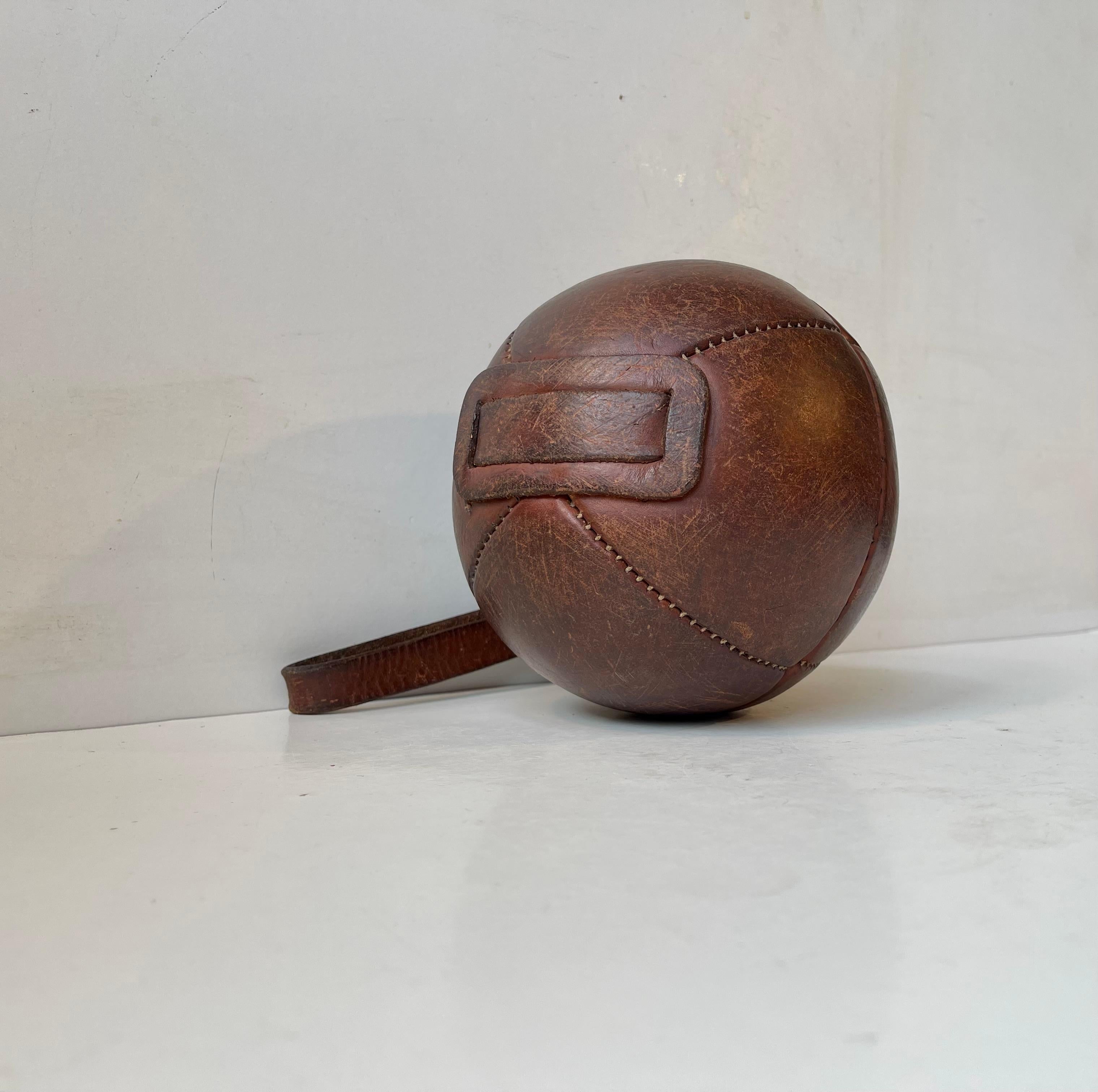 A decorative strapped ball in patinated tanned leather. These were originally used as a sling, a medical or a boxing ball. This example was handmade in France circa 1930-40 and its in a very authentic and satisfying condition. Measurements: H/L: 39
