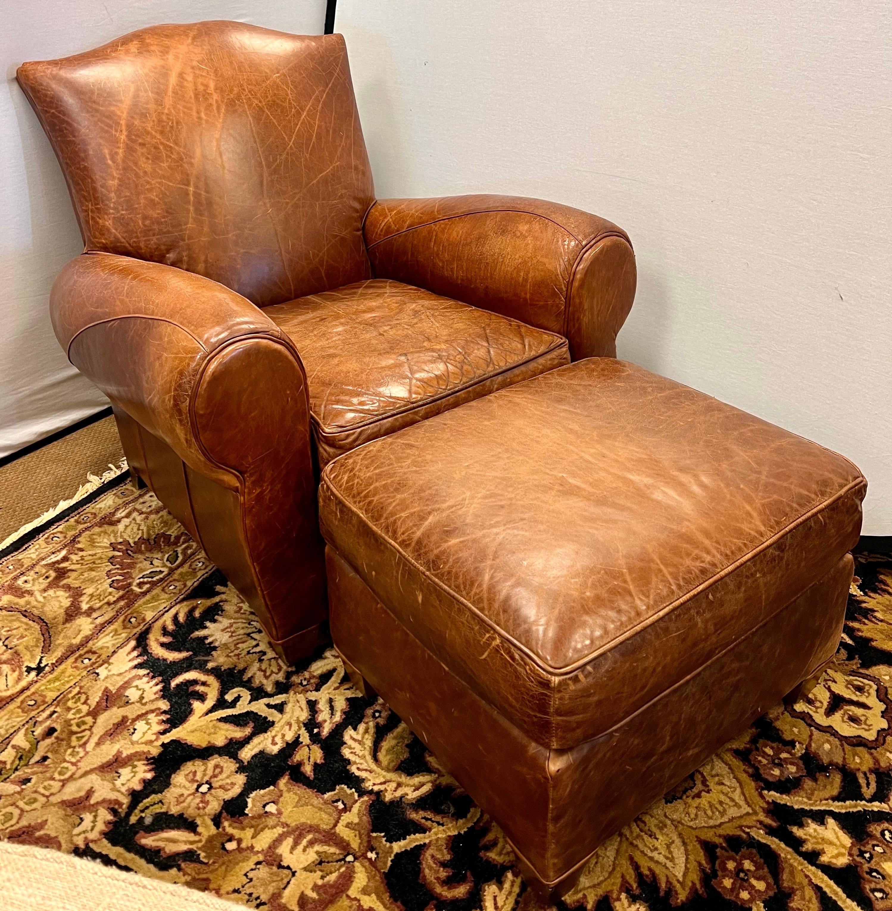 Vintage French mustache back club chair with matching ottoman, that have been aged to perfection with coveted distressed patina only acquired through age and use. The leather is a luxurious caramel brown. The chair is oversized and structurally