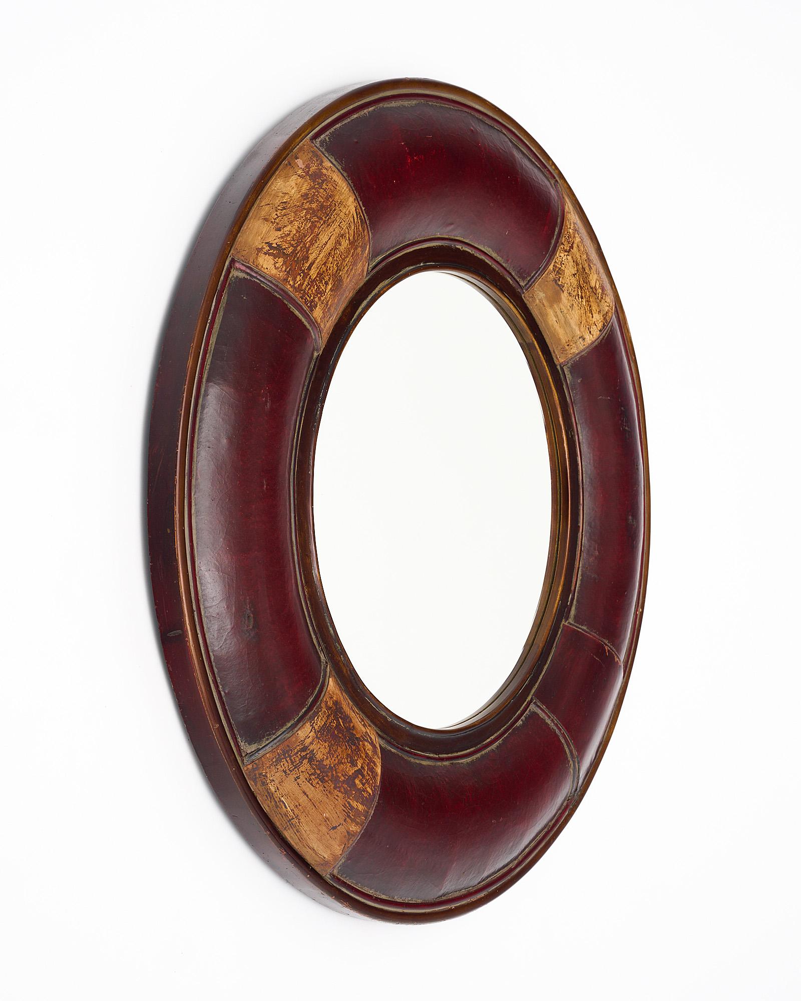 Miroir français composé d'un cadre circulaire recouvert de cuir marron. Cette pièce unique présente des accents dorés à la feuille et un miroir circulaire central.
